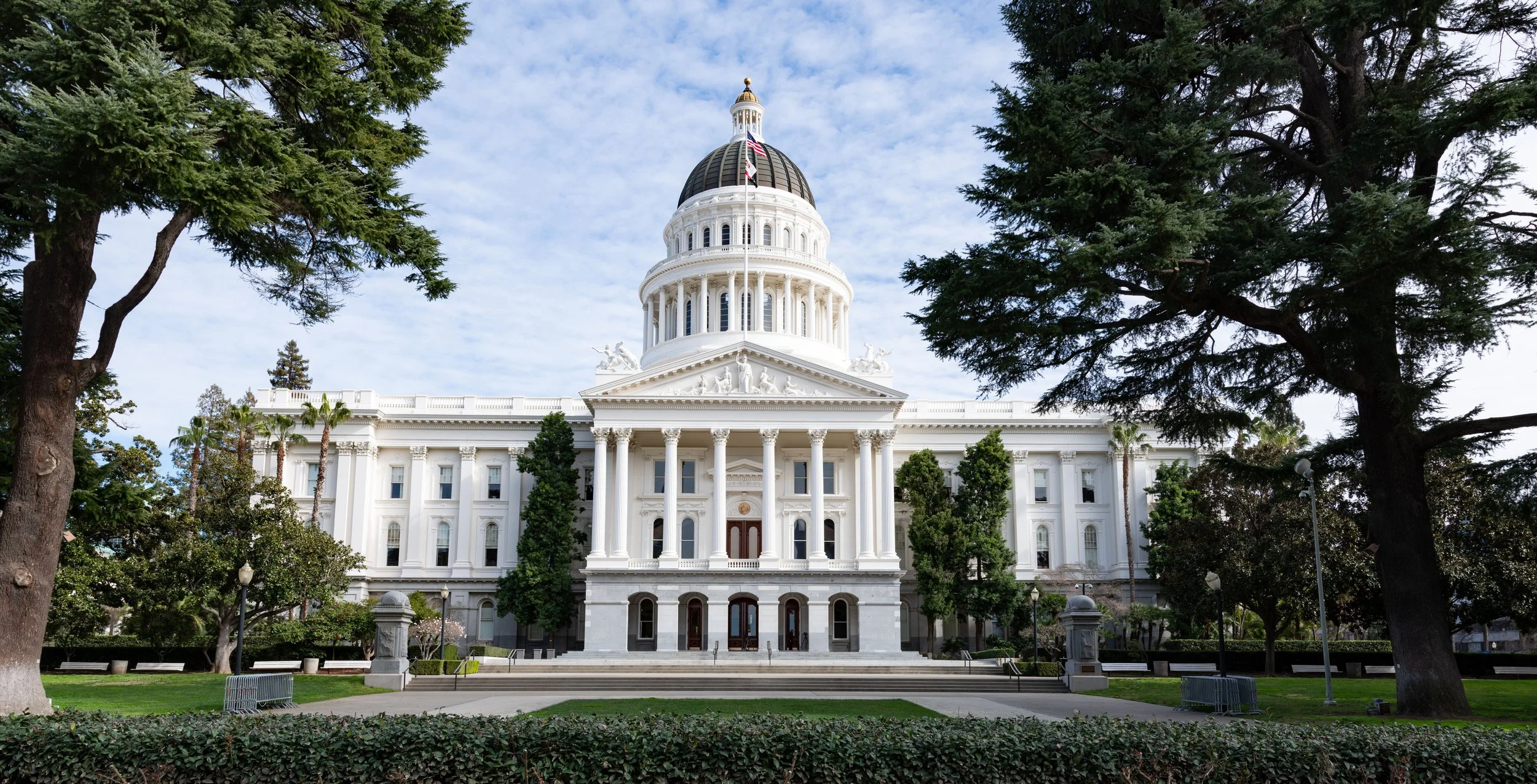 Photograph of the California State Capitol building in Sacramento, surrounded by trees and a lawn.