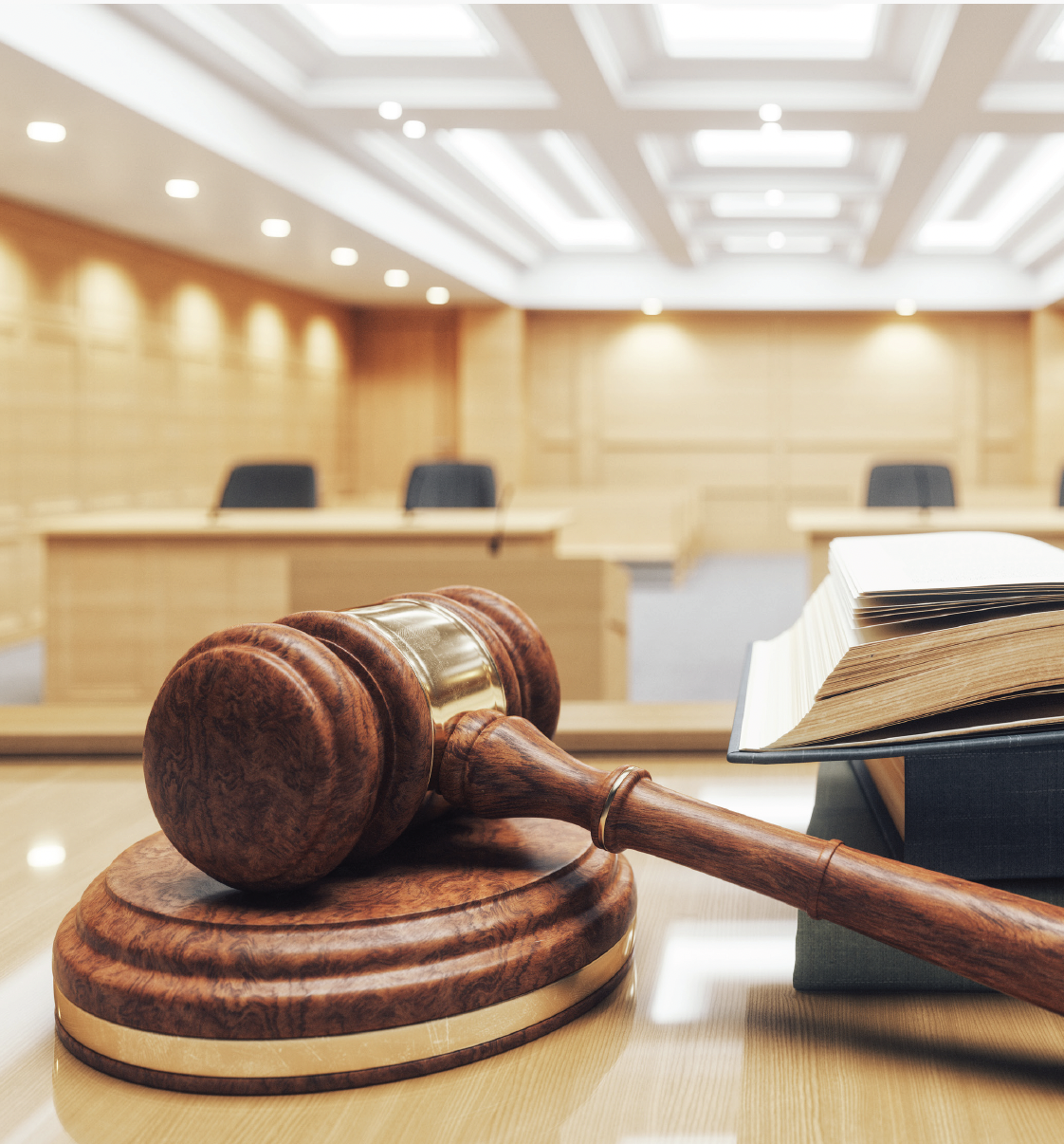 Gavel and legal book on a table in a courtroom or legal setting with wood-paneled walls and chairs in the background.