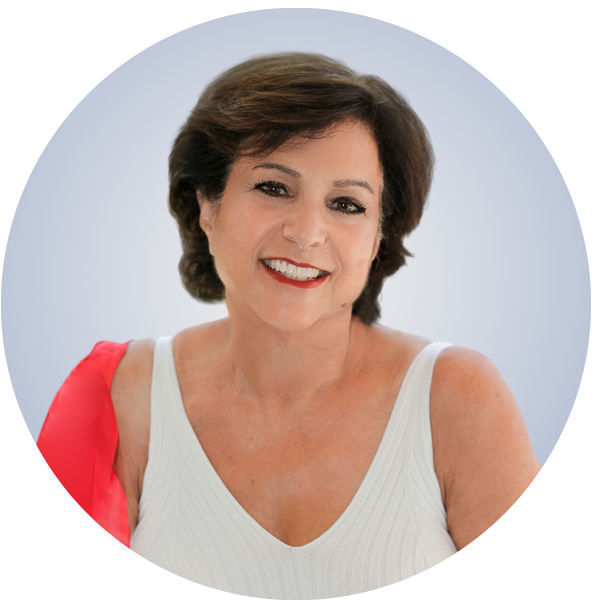 A smiling middle-aged woman with short brown hair wearing a white top and a red shawl against a light blue background.