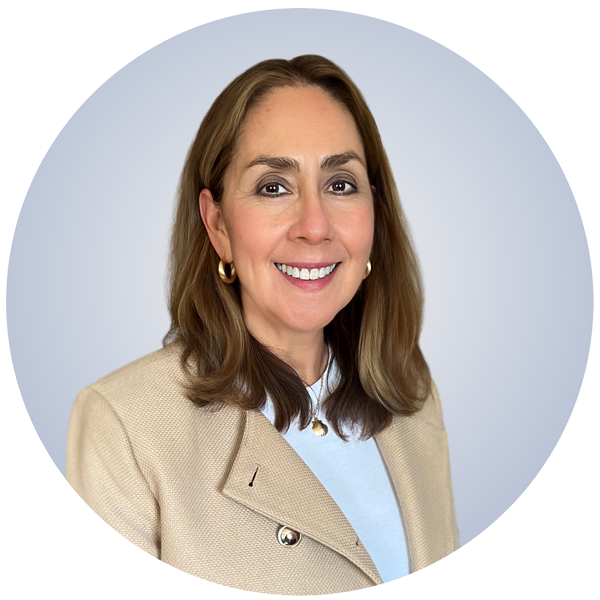 A woman with shoulder-length brown hair, wearing a beige blazer over a light blue top, smiling, against a gray background