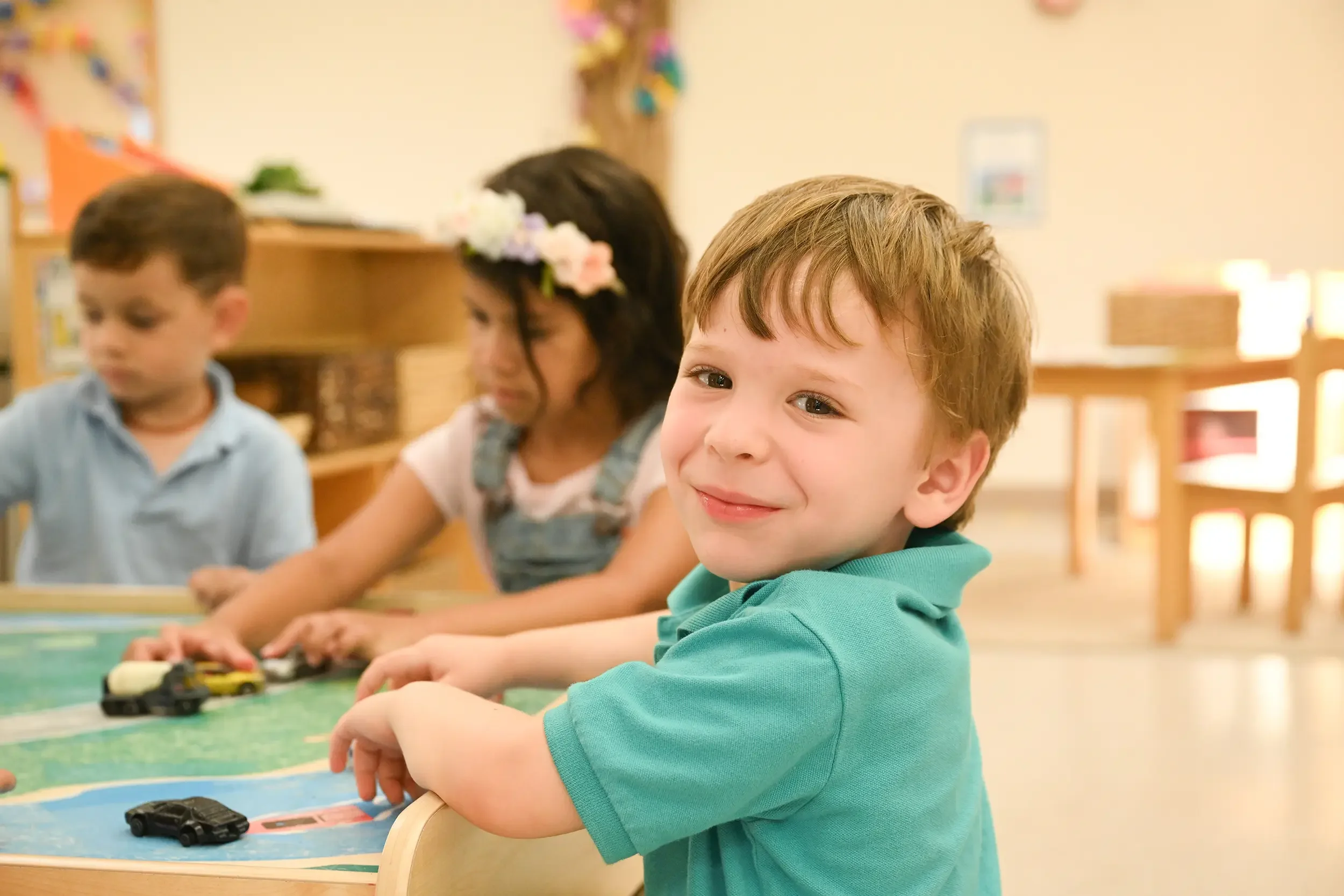 Children playing with toy cars in a classroom, smiling and enjoying their activity.