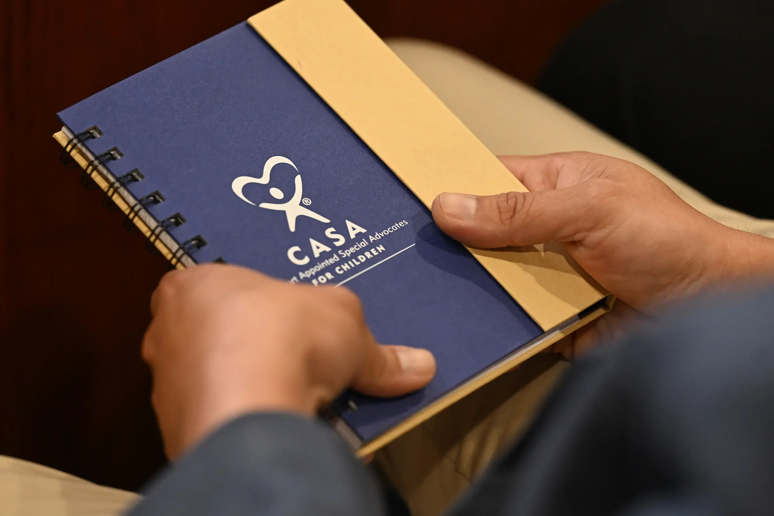 Close-up of someone holding a blue spiral-bound notebook with the CARES Act logo and text, partially covered by a yellow paper, with hands visible.