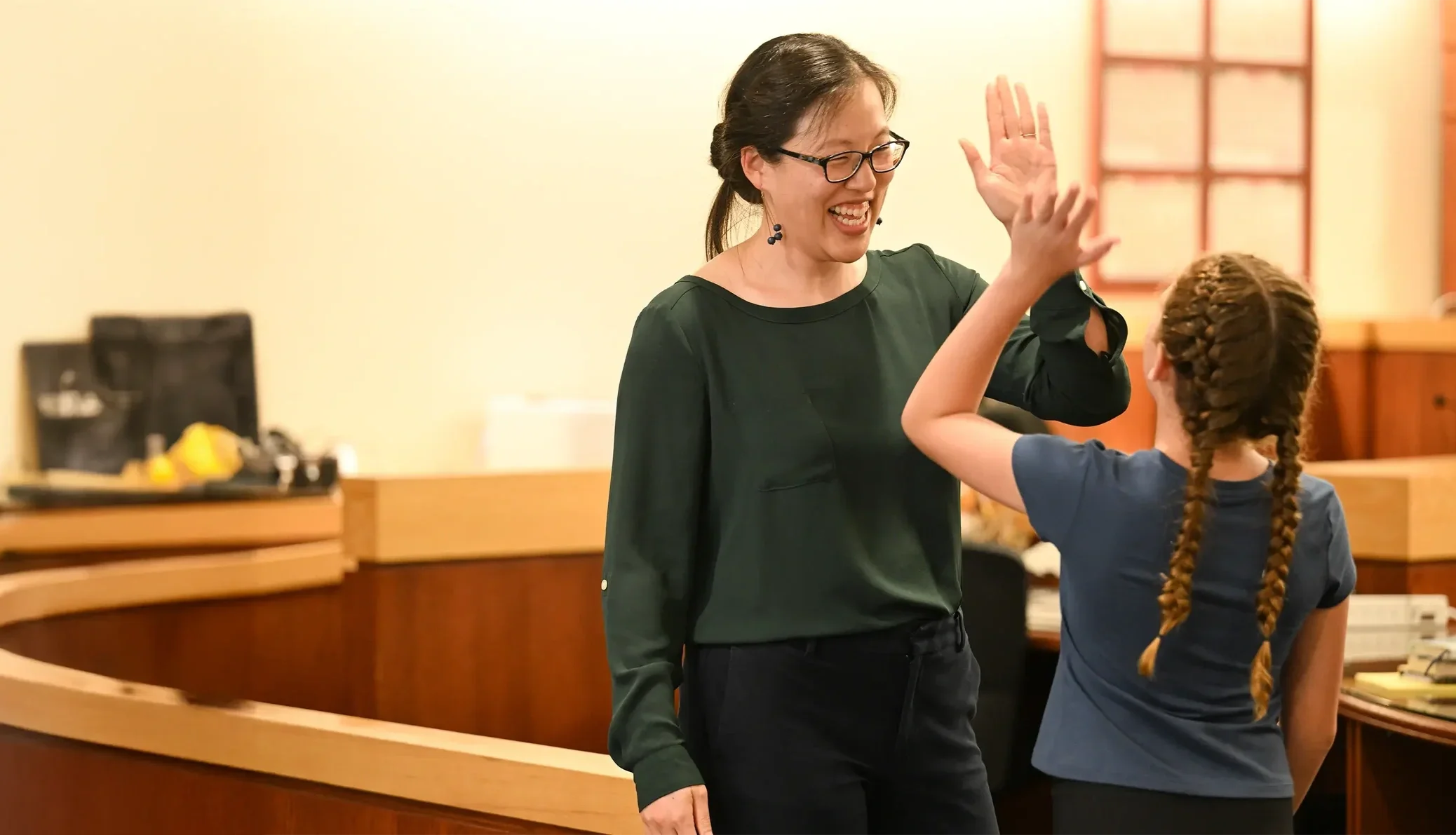 A woman and a girl giving each other a high five in a room with warm lighting.