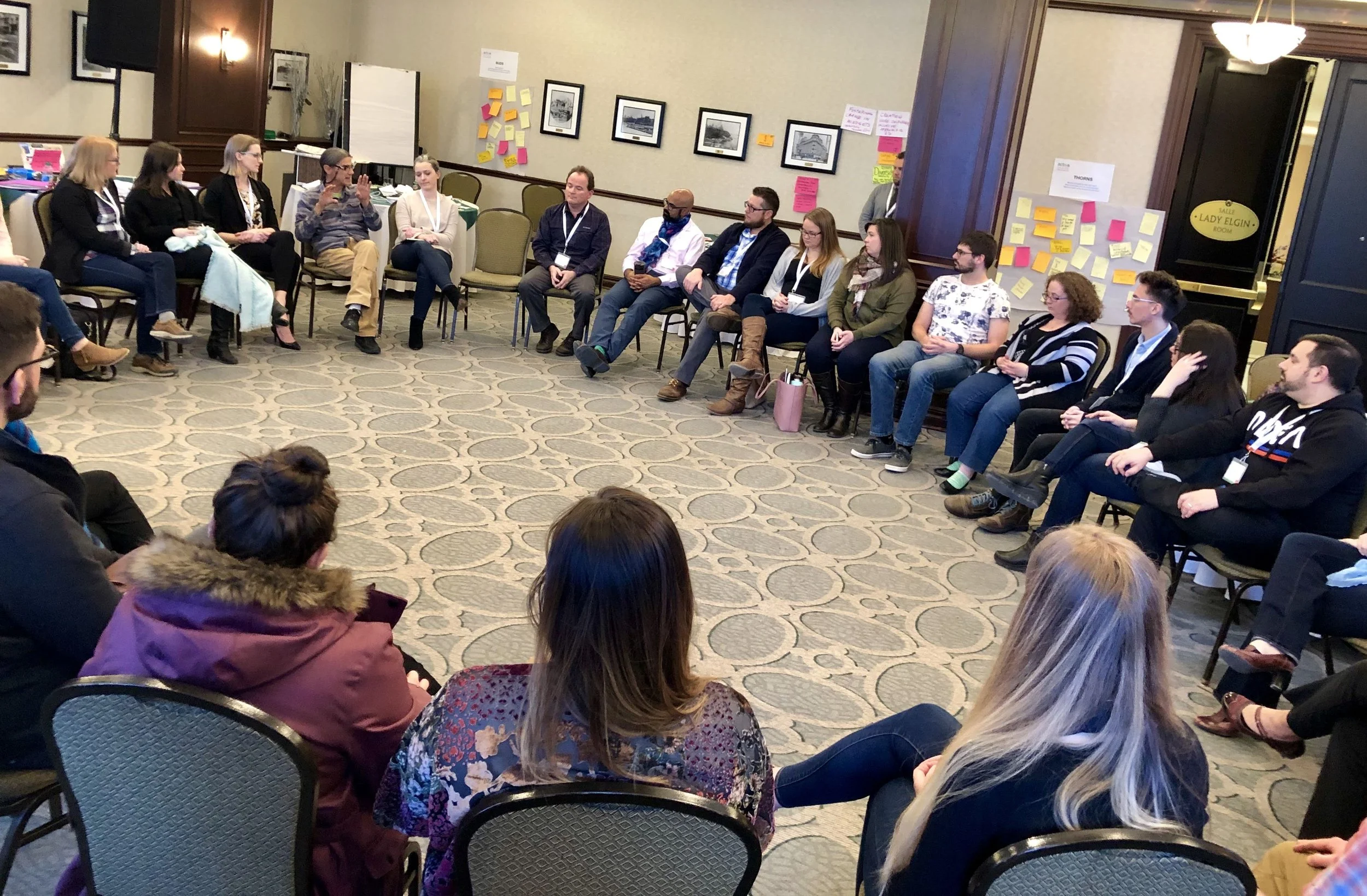 Group of people sitting in a circle in a conference room, participating in a discussion or workshop.