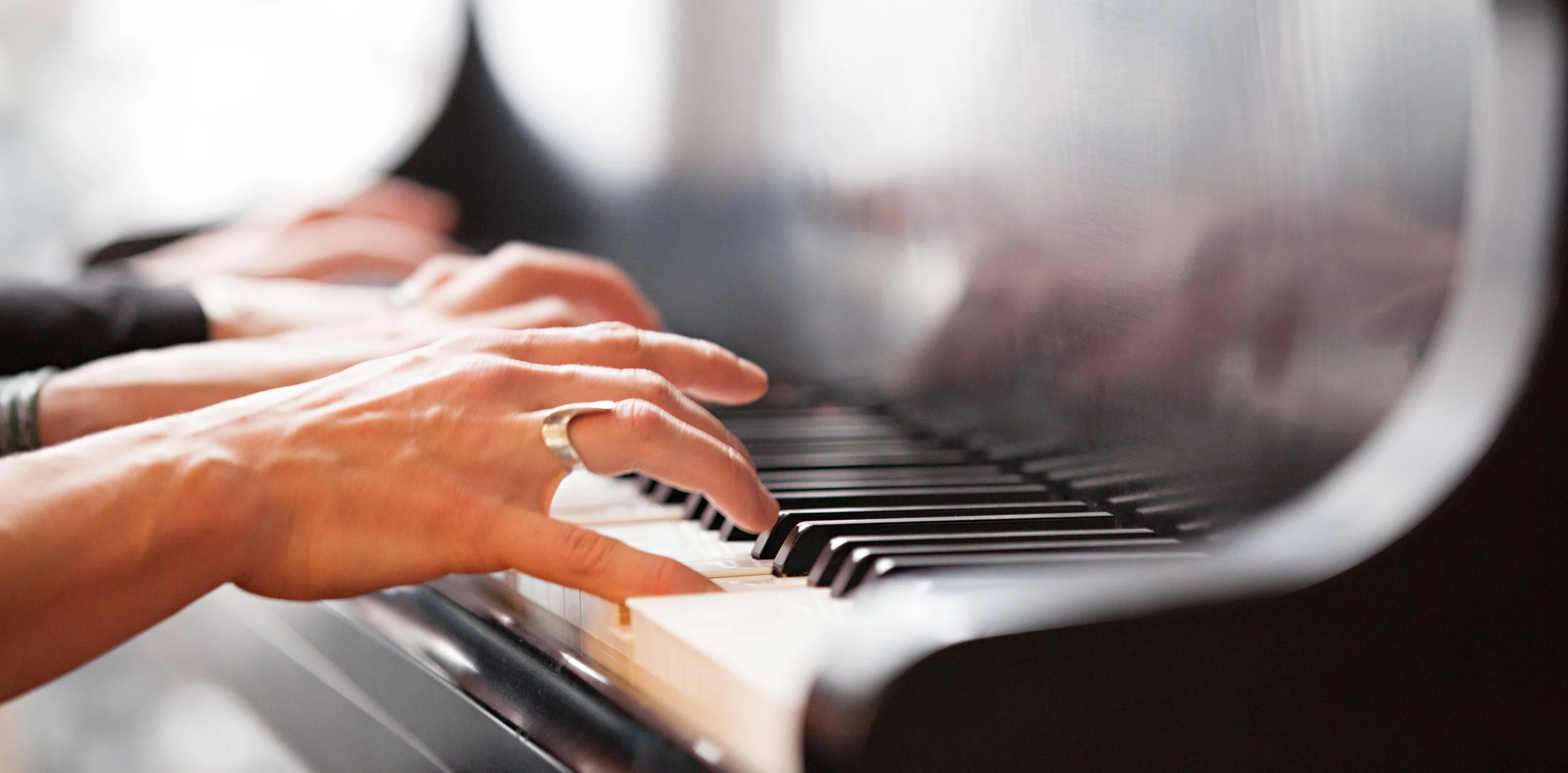 Close-up of hands playing the piano, focusing on fingers pressing the keys, with a blurred background.