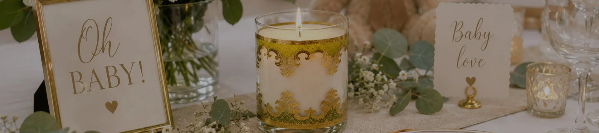 Decorative table setting with a candle, baby-themed signs, and floral accents, celebrating pregnancy or upcoming birth.