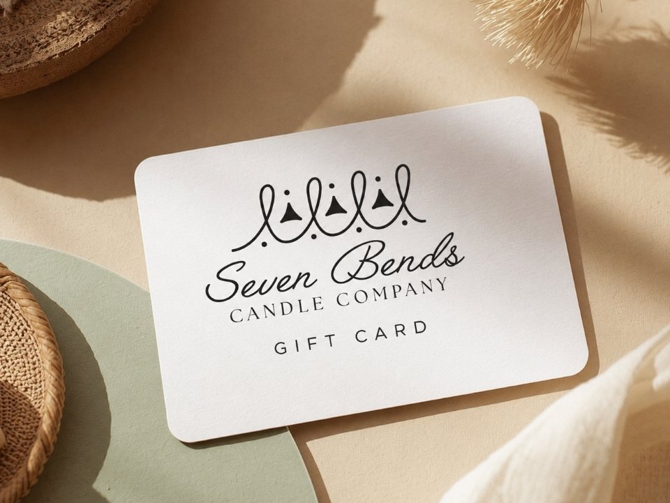 A gift card from Seven Bends Candle Company with a crown illustration and elegant black text, placed on a beige surface with surrounding decorative objects.