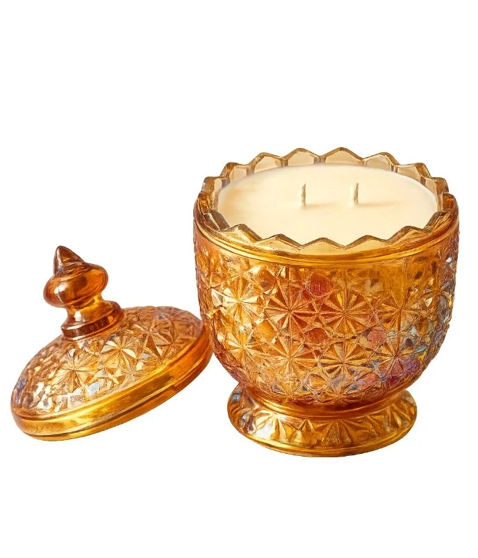 Amber-colored glass candle holder with a lid, containing a white candle and decorated with a geometric pattern.