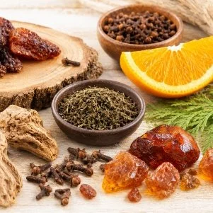 Assorted spices, dried fruits, and a slice of orange on a wooden surface.