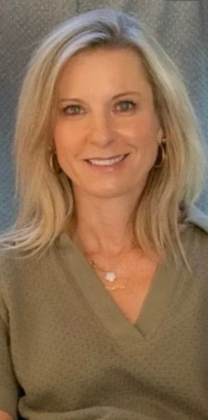 A middle-aged woman with blonde hair smiling, wearing a light green top and gold jewelry.