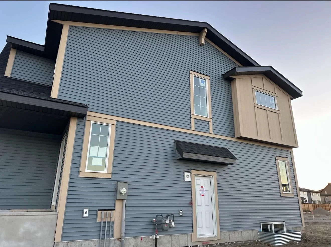 New multi-story house with blue siding, beige trim, multiple windows, and construction signs, in a residential area under construction.