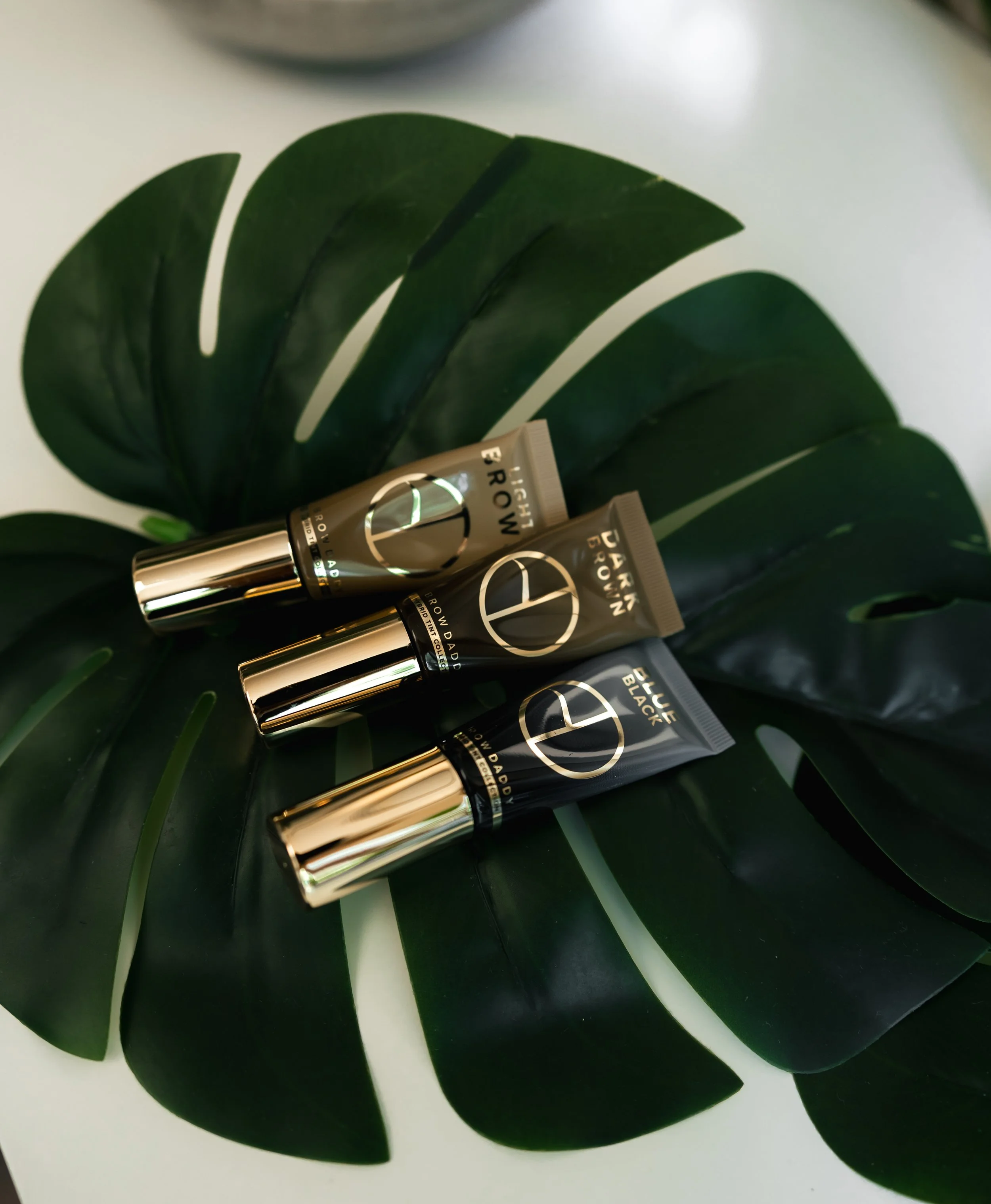 Three tubes of skincare product labeled B Youth Dawn, placed on a dark green monstera leaf.