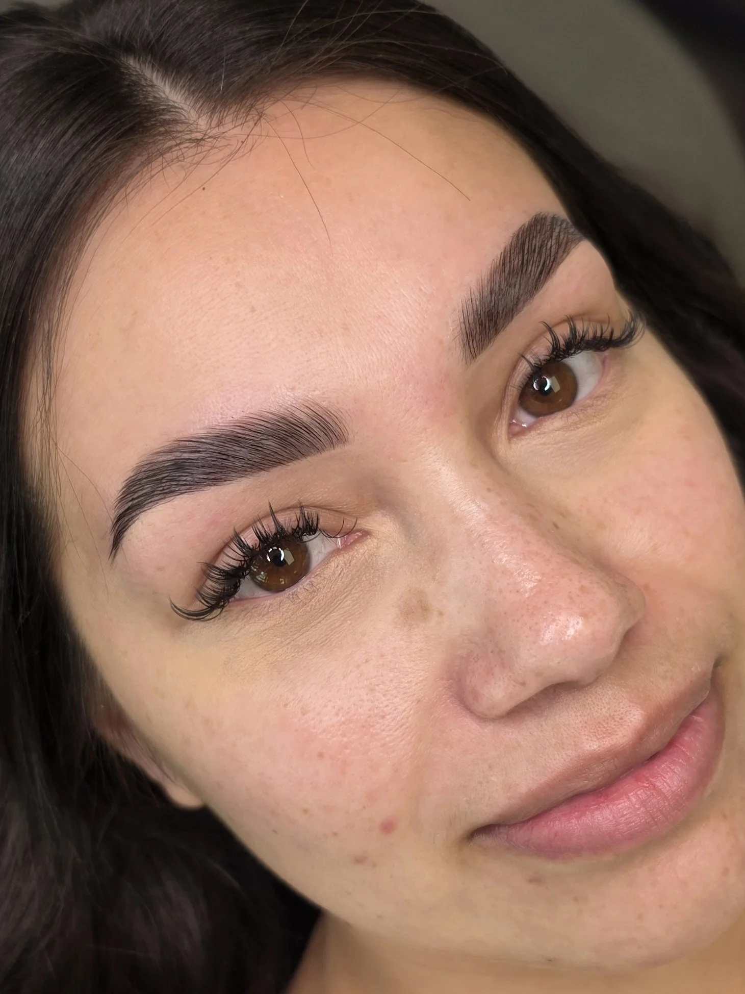 Close-up of a woman's face showing well-groomed eyebrows, brown eyes with long eyelashes, and clear skin with a few freckles.