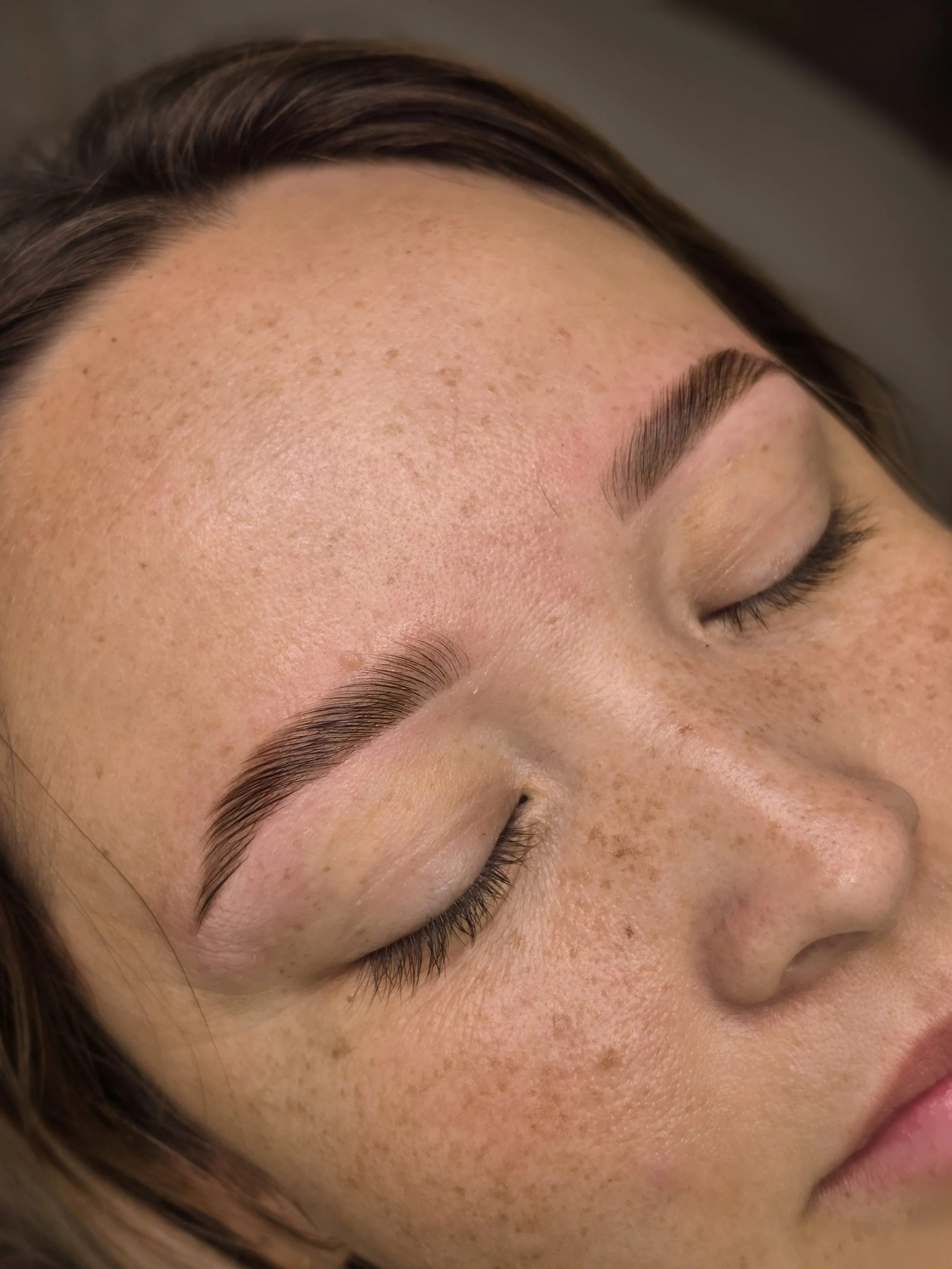 Close-up of a woman's face showing her closed eyes, well-groomed eyebrows, and freckled skin.