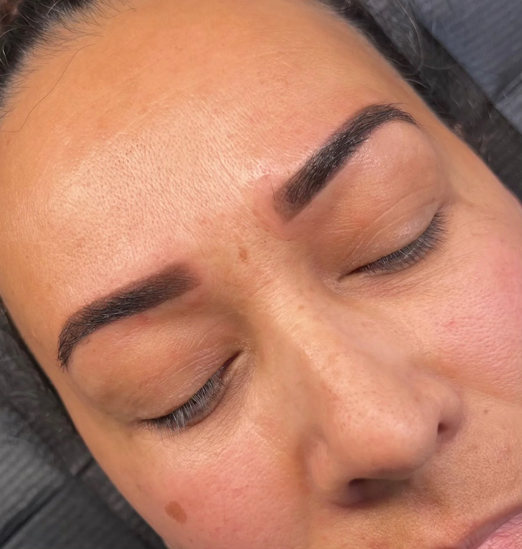 Close-up of a woman with well-groomed eyebrows, natural skin texture, and closed eyes showing her eyelashes.