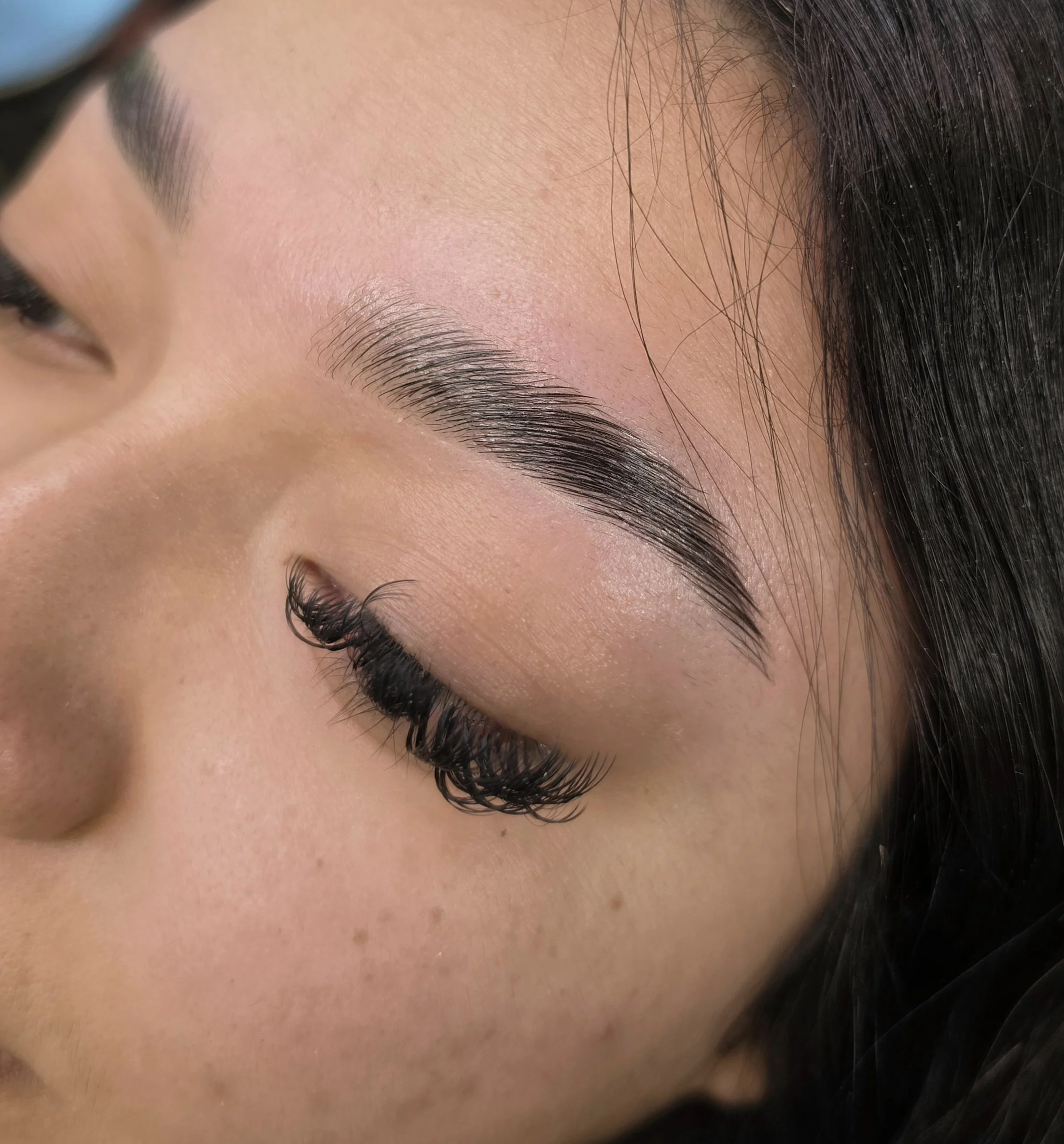Close-up of a person's face showing closed eyes with well-groomed eyebrows, long eyelashes, and smooth skin.