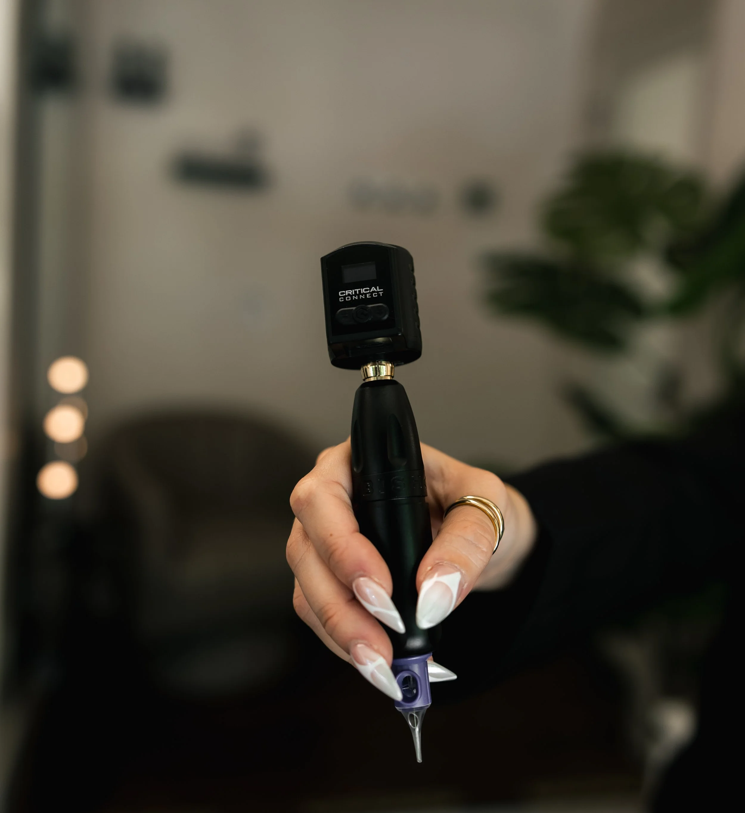 A person holding a black medical device labeled 'Critical Connect,' with a nozzle and a droplet of liquid dripping from it, in a room with blurred background.