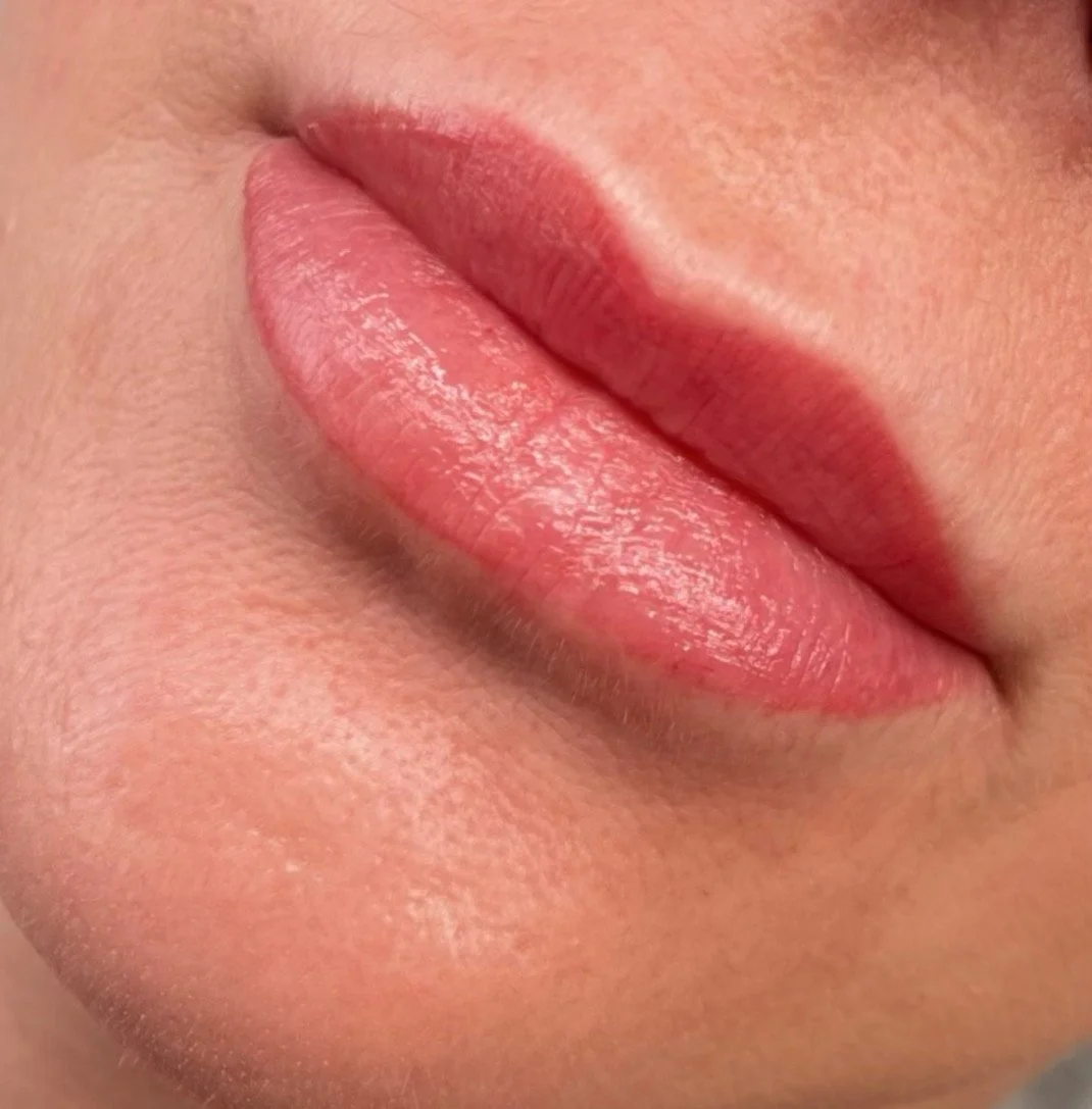Close-up of a person's lips with pink lipstick, showing their natural texture and smooth skin surrounding the lips.
