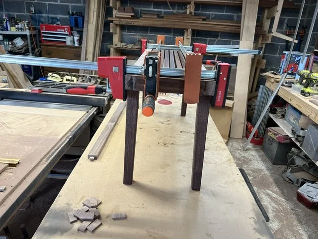 Mid-century modern entryway bench with splayed legs. On workbench, in clamps during final  glue-up.