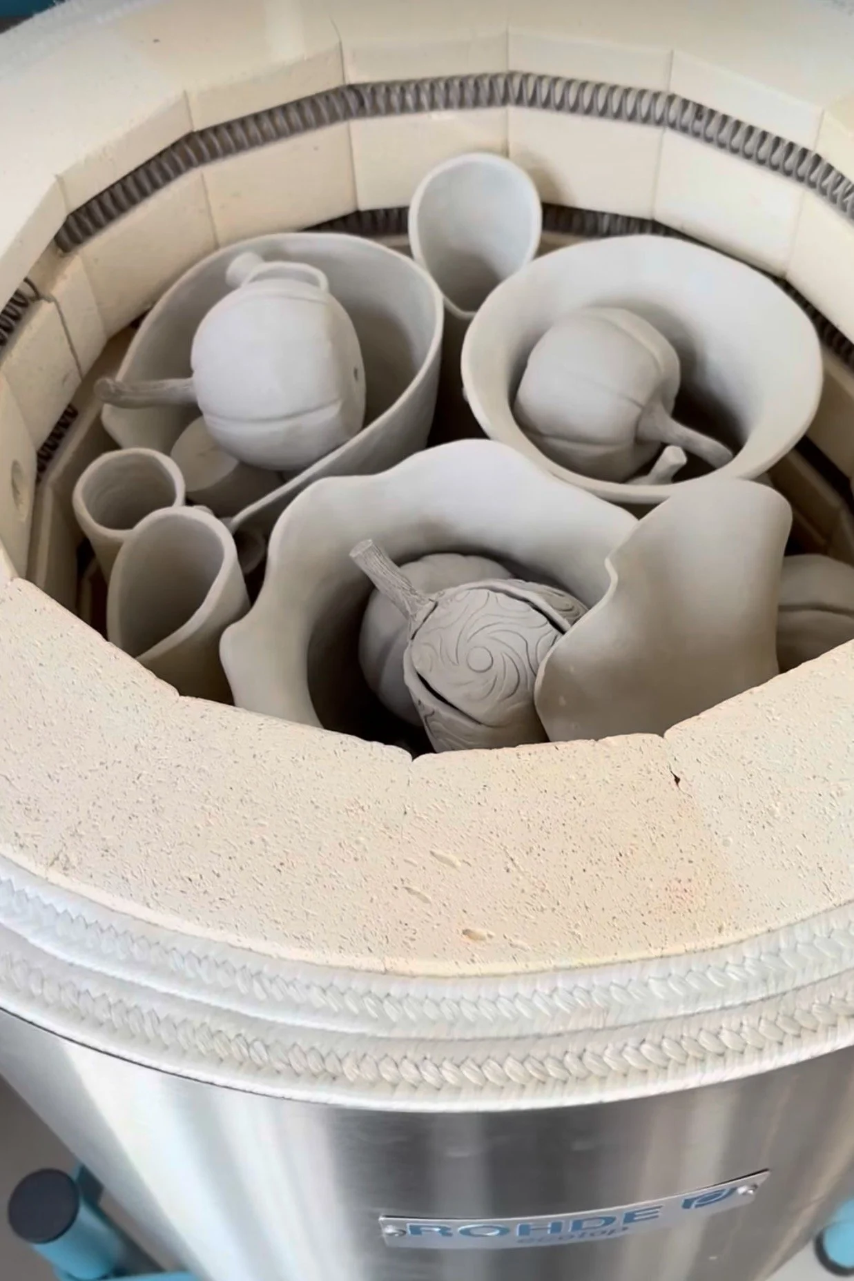 Handmade ceramic pieces inside the pottery kiln ready for firing.