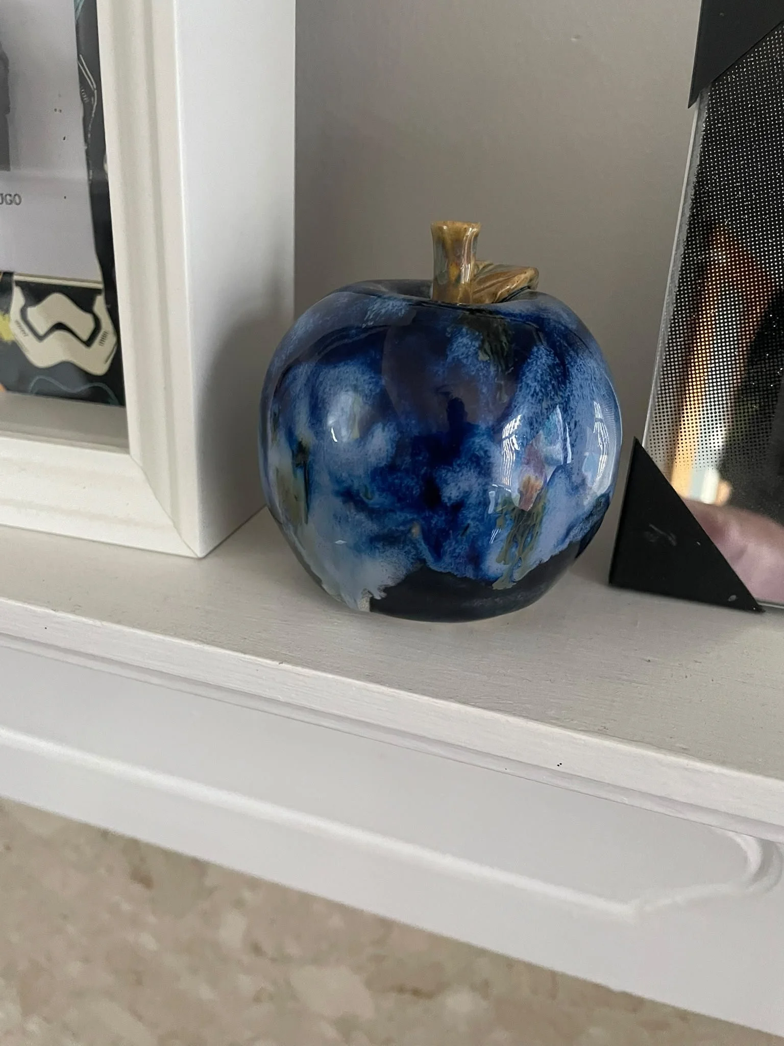 Handcrafted blue glazed ceramic apple displayed on a shelf.
