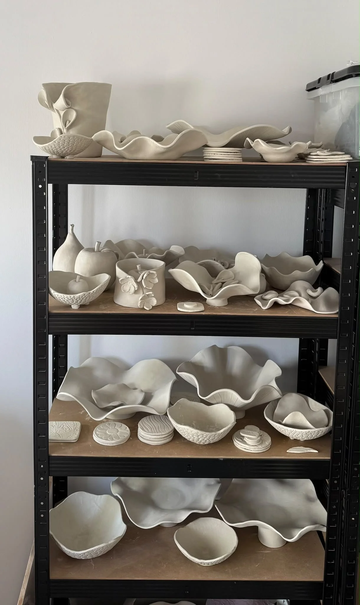 Shelves of handmade unglazed ceramic pieces waiting to be fired in the pottery studio.