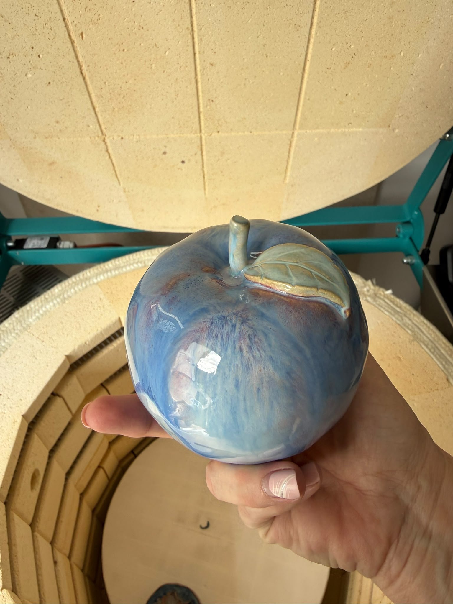 Handcrafted blue glazed ceramic apple held in the hand.