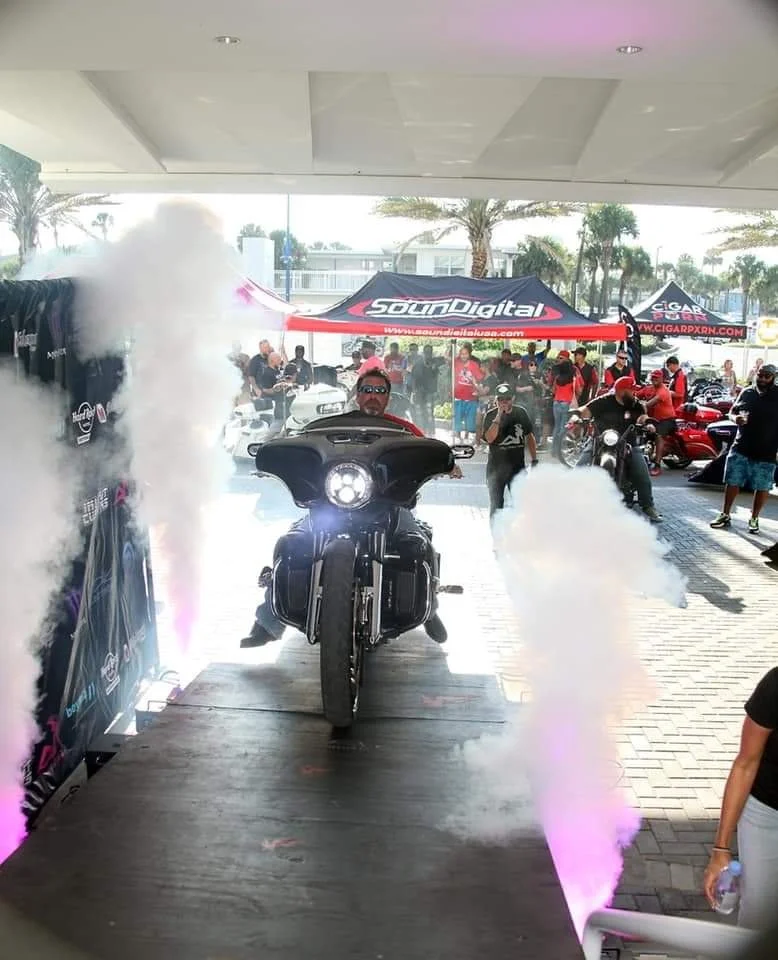 Paul DeGregorio riding a custom motorcycle at a motorcycle audio competition event, showcasing award-winning sound system design and tuning expertise developed through decades of competition experience.