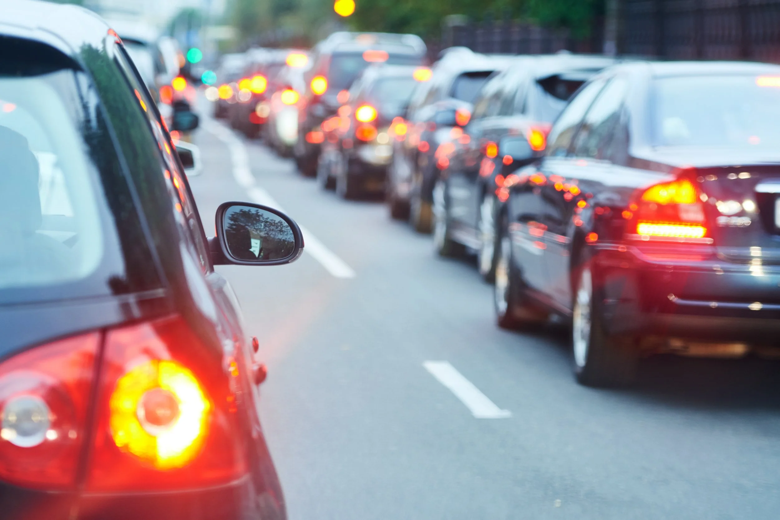 Une file de voitures en arrêt ou en ralentissement, avec des feux arrière rouges allumés sur une route urbaine, vue de l'arrière d'une voiture rouge.