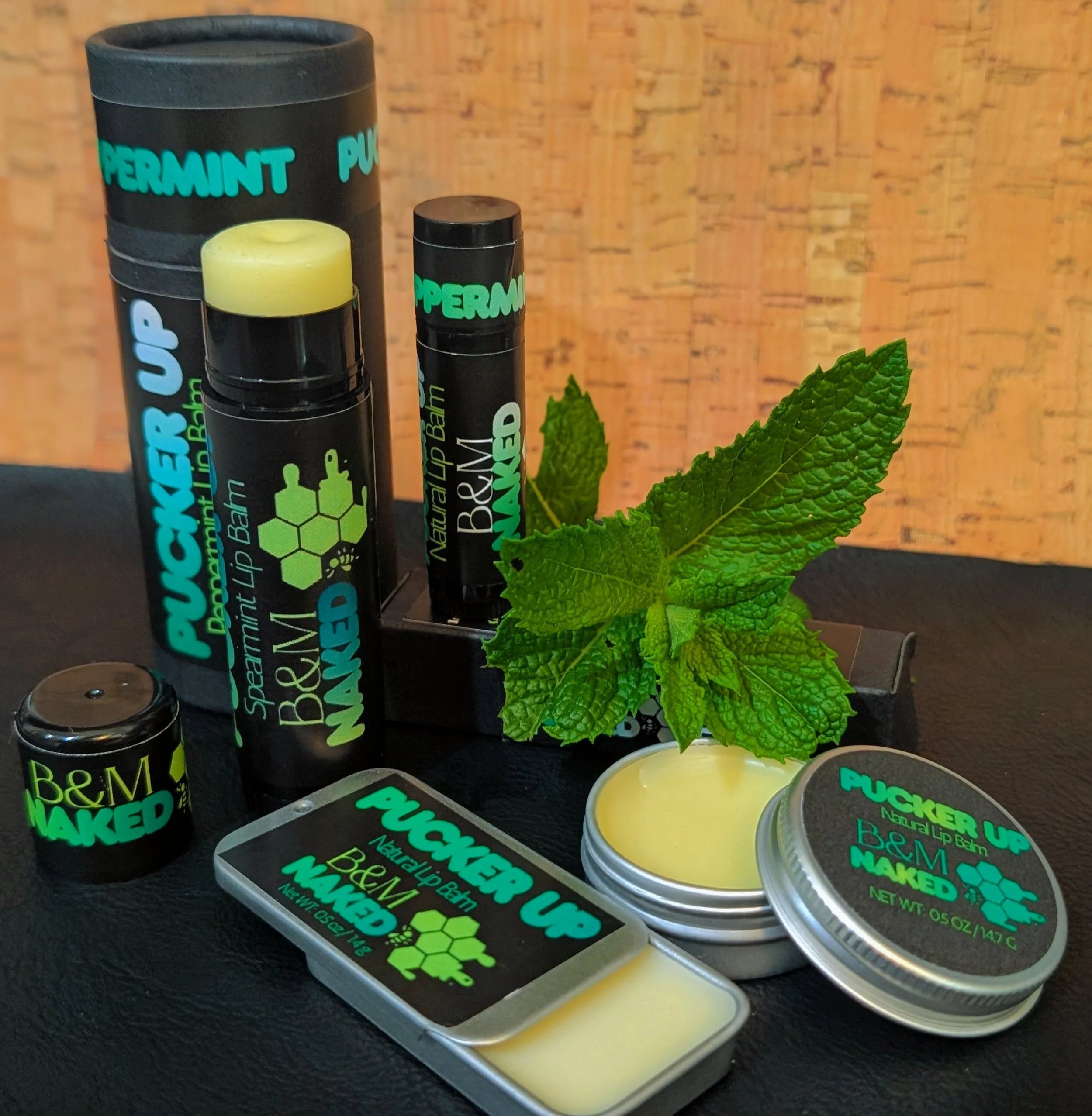 Lip balm containers with black labels, green text, and mint leaves in the foreground, set against a wooden background.