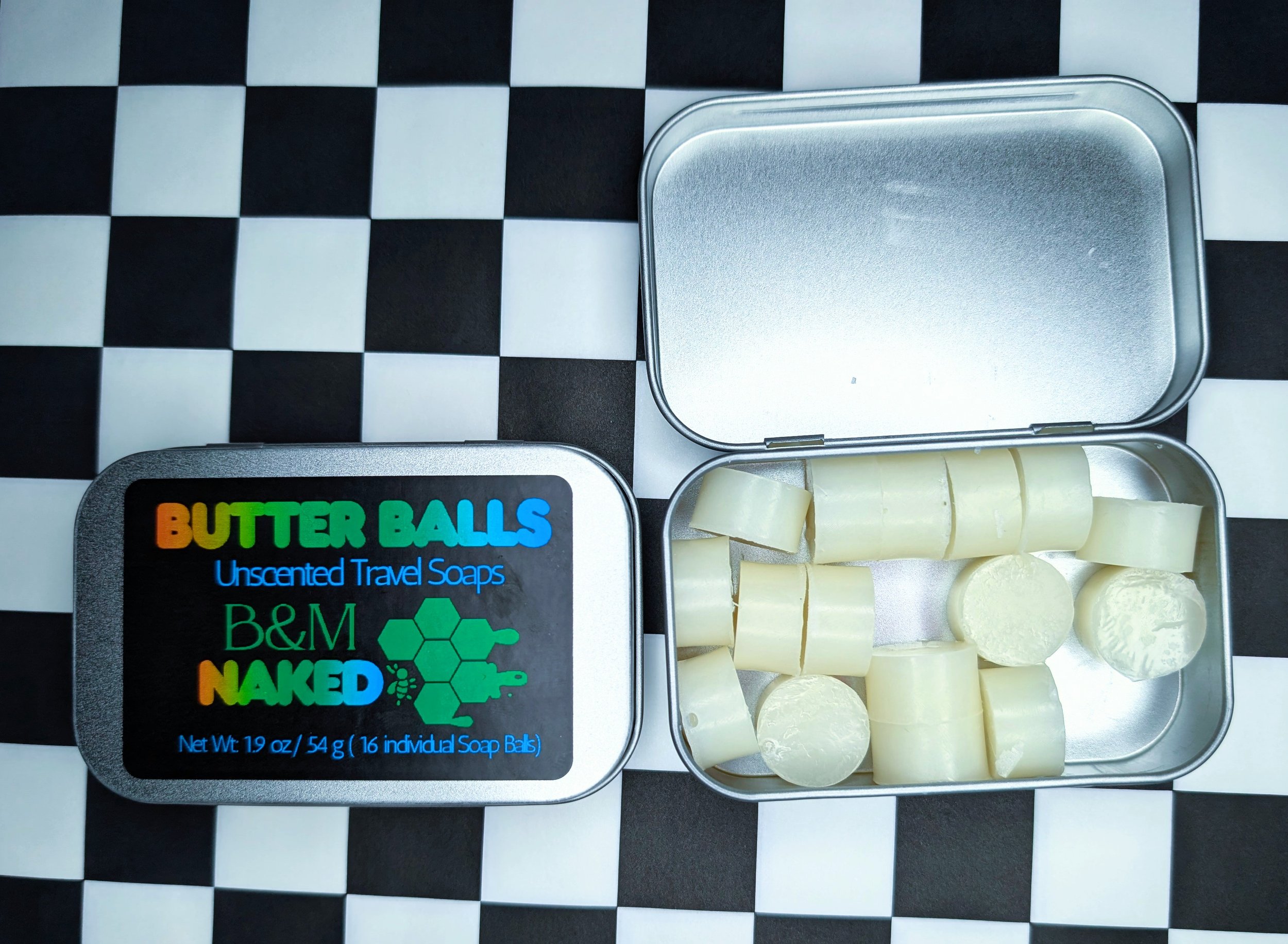 Open metal tin containing small white soap bars on a black and white checkered surface.
