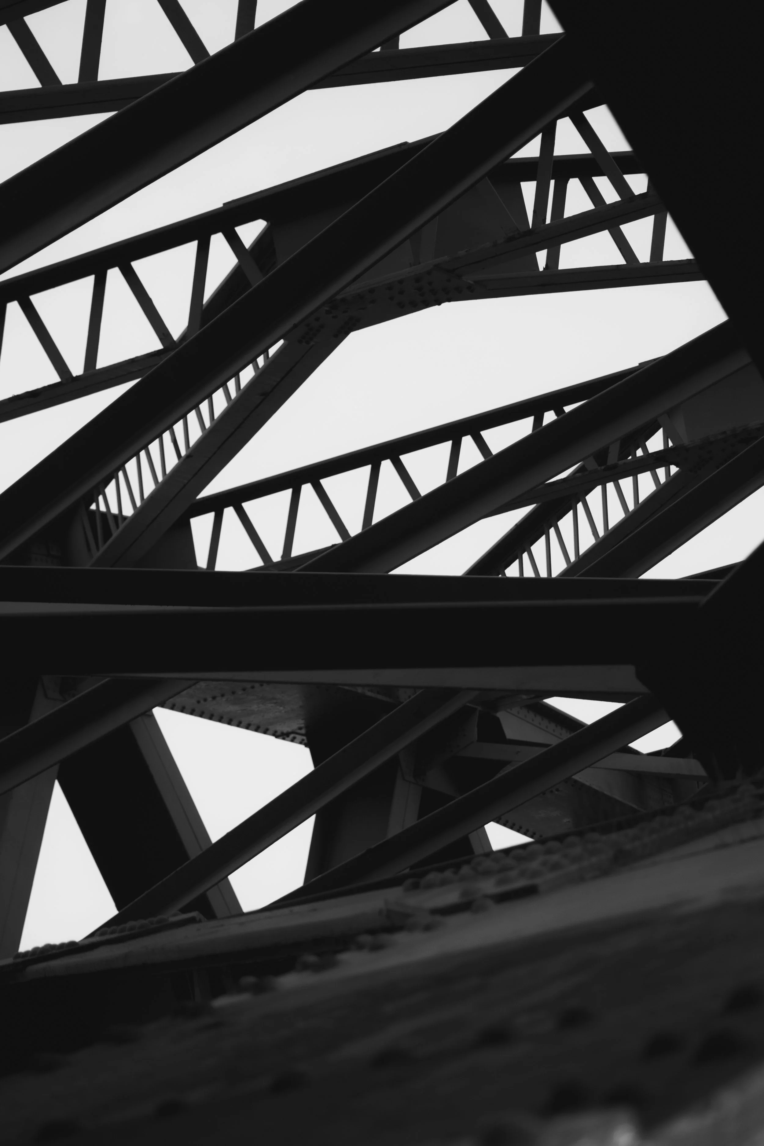 Close-up black and white photo of a steel bridge under construction, showcasing the intricate framework and supporting beams.