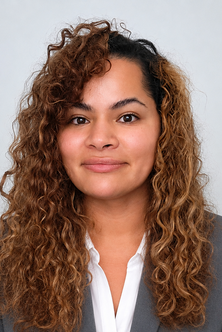 A woman with long, curly brown hair, wearing a gray blazer and white shirt, smiling softly against a plain background.