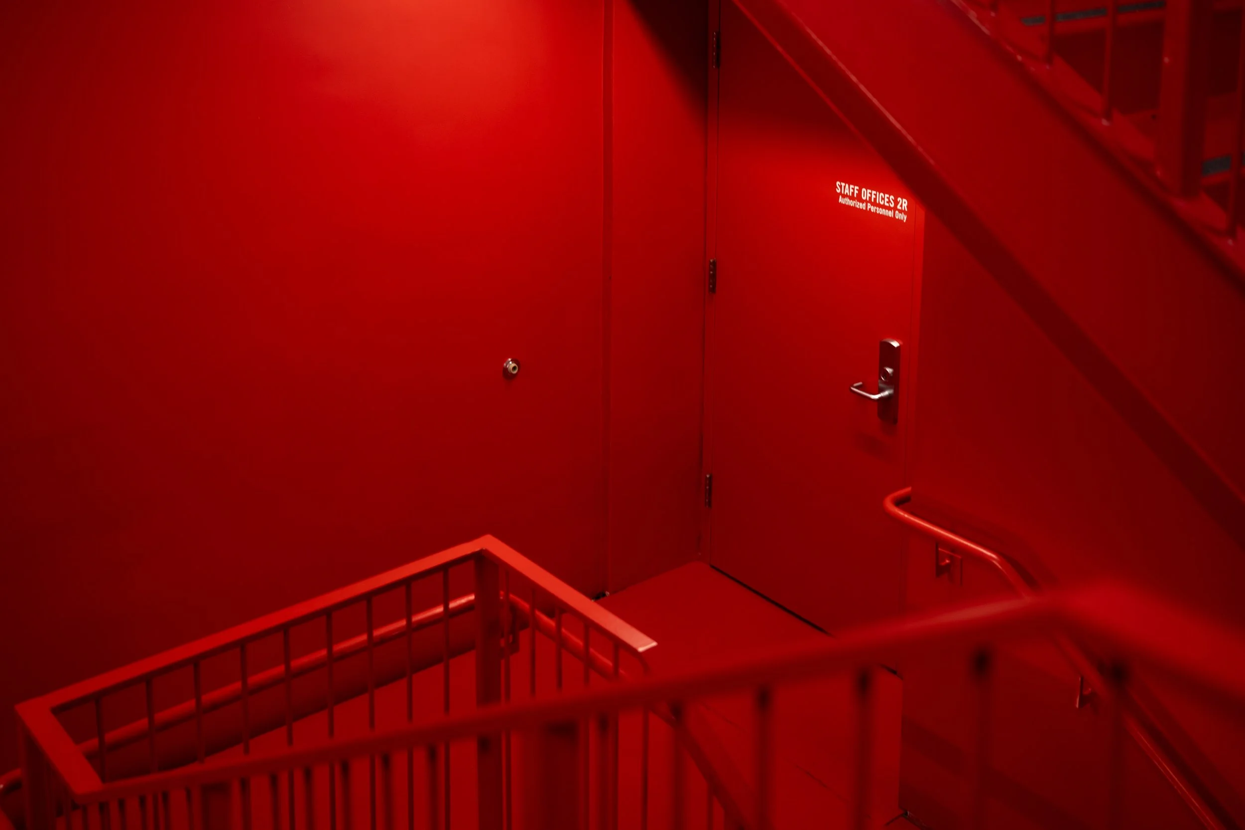 Red stairway and landing area with a door labeled "STAFF OFFICES 2R" and railings.