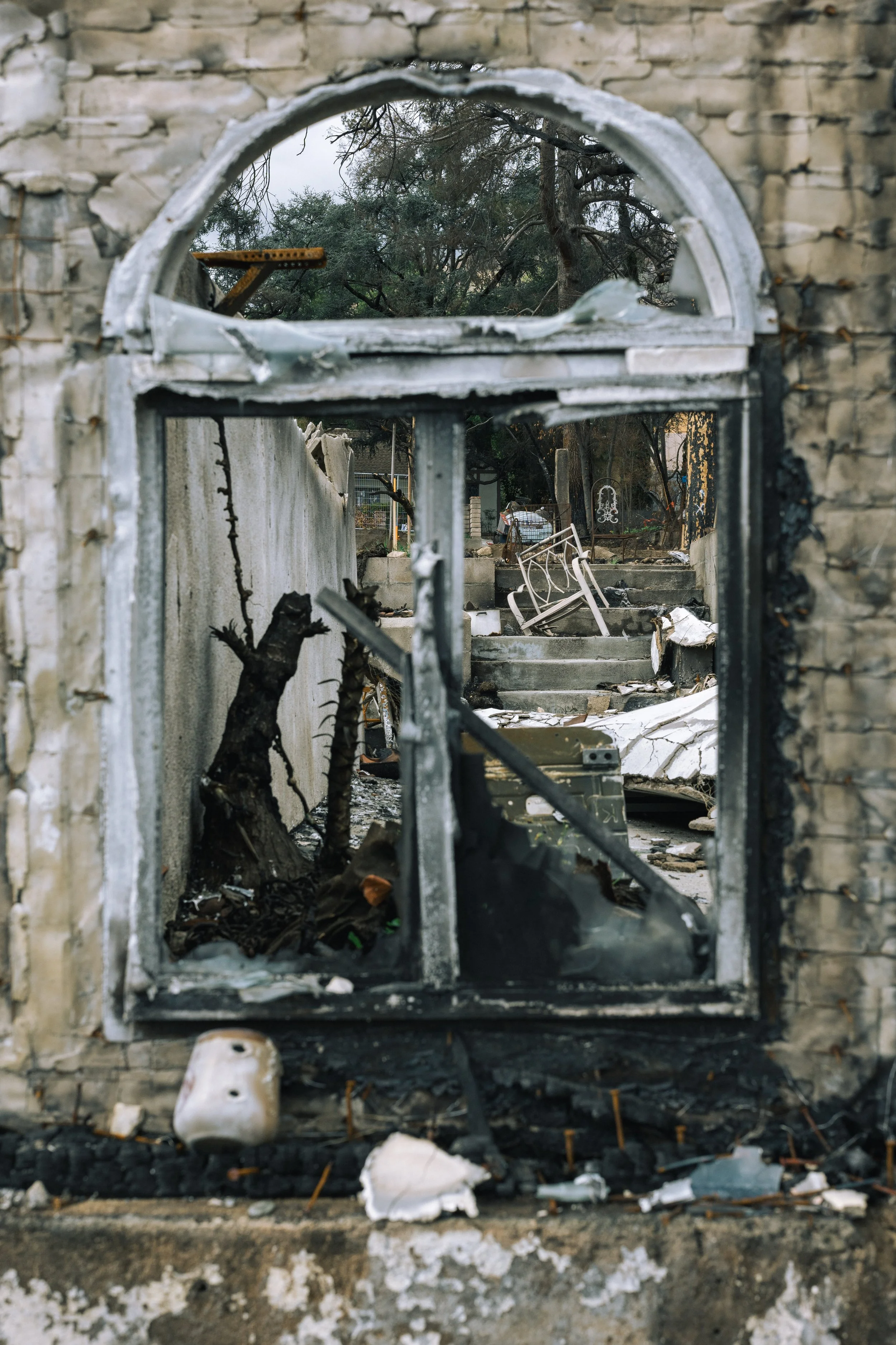 Destroyed window with charred frame looking into a burned area with collapsed furniture and burnt debris.
