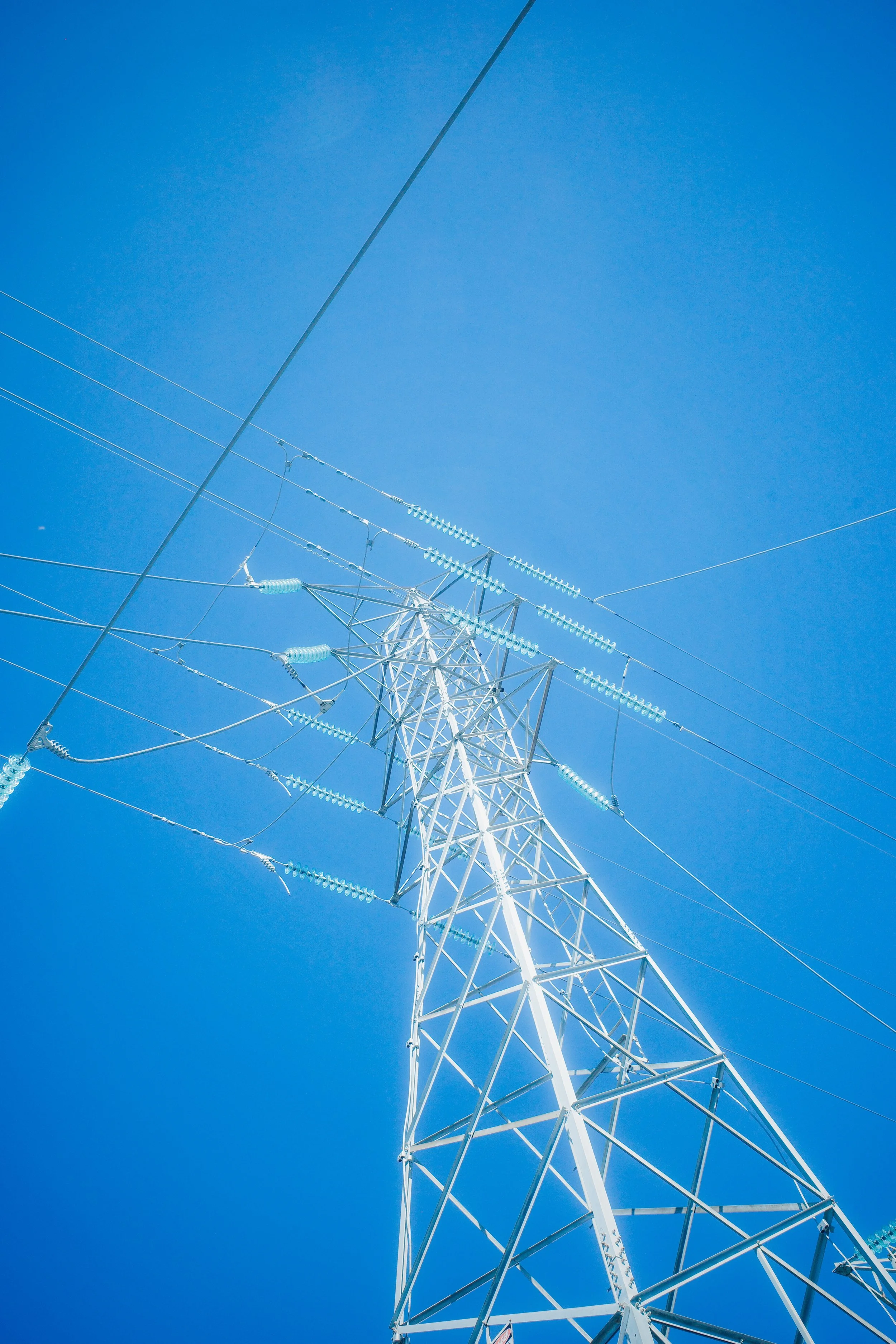 A white electrical transmission tower with power lines against a clear blue sky.
