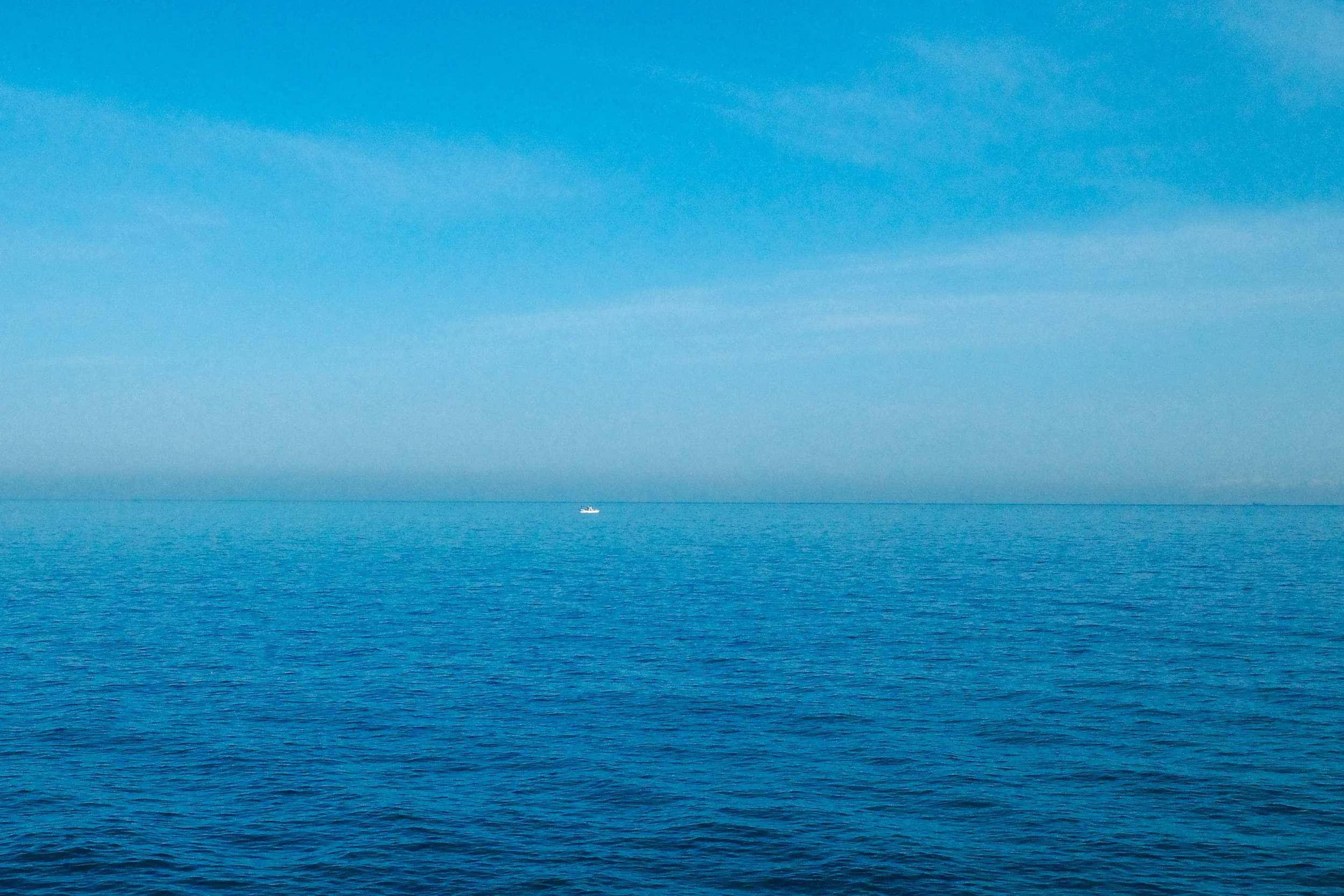 A small boat floating on the calm blue ocean with a clear sky above.