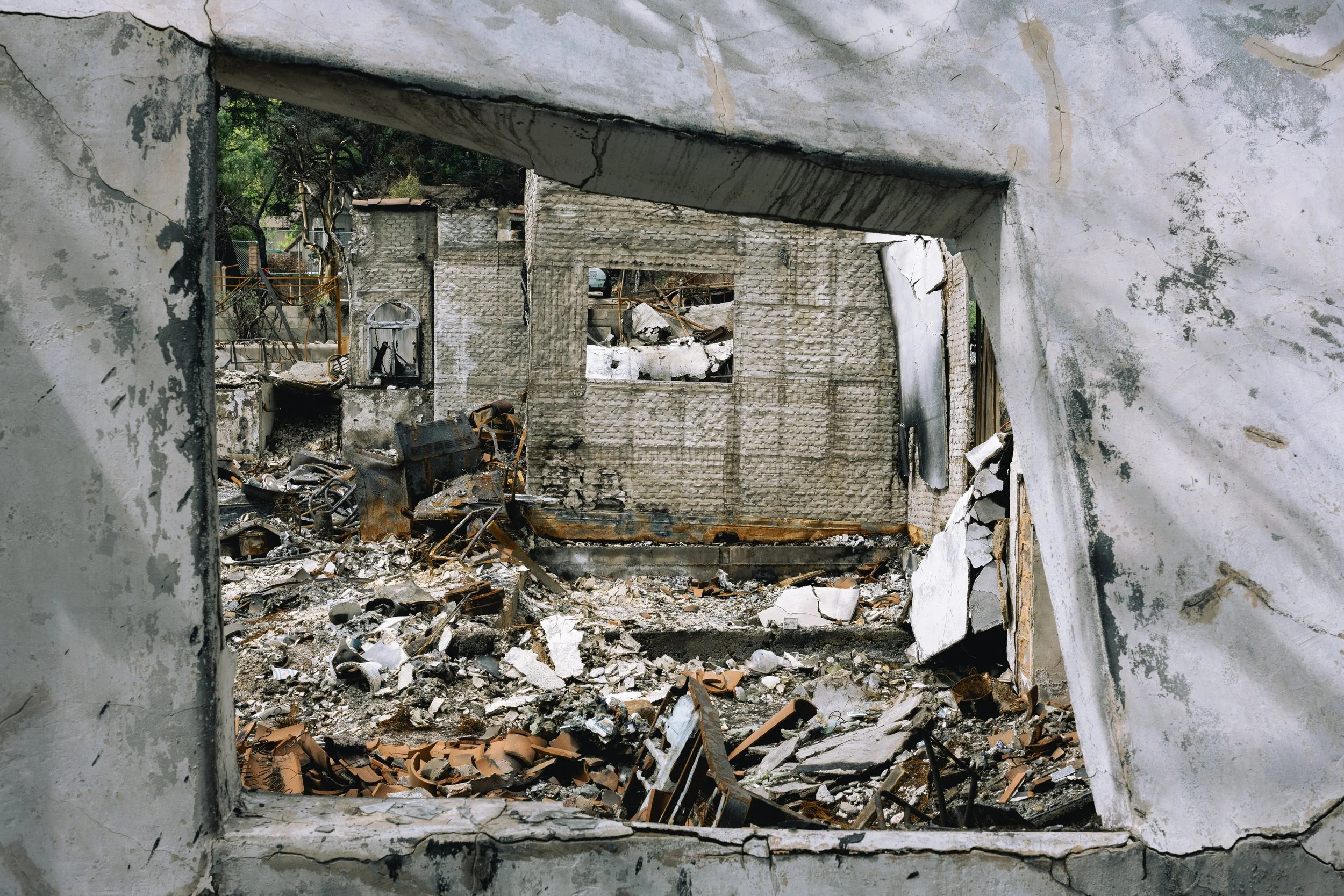 View of a burned and destroyed building through a large, broken window frame, with debris and charred remains scattered on the ground.