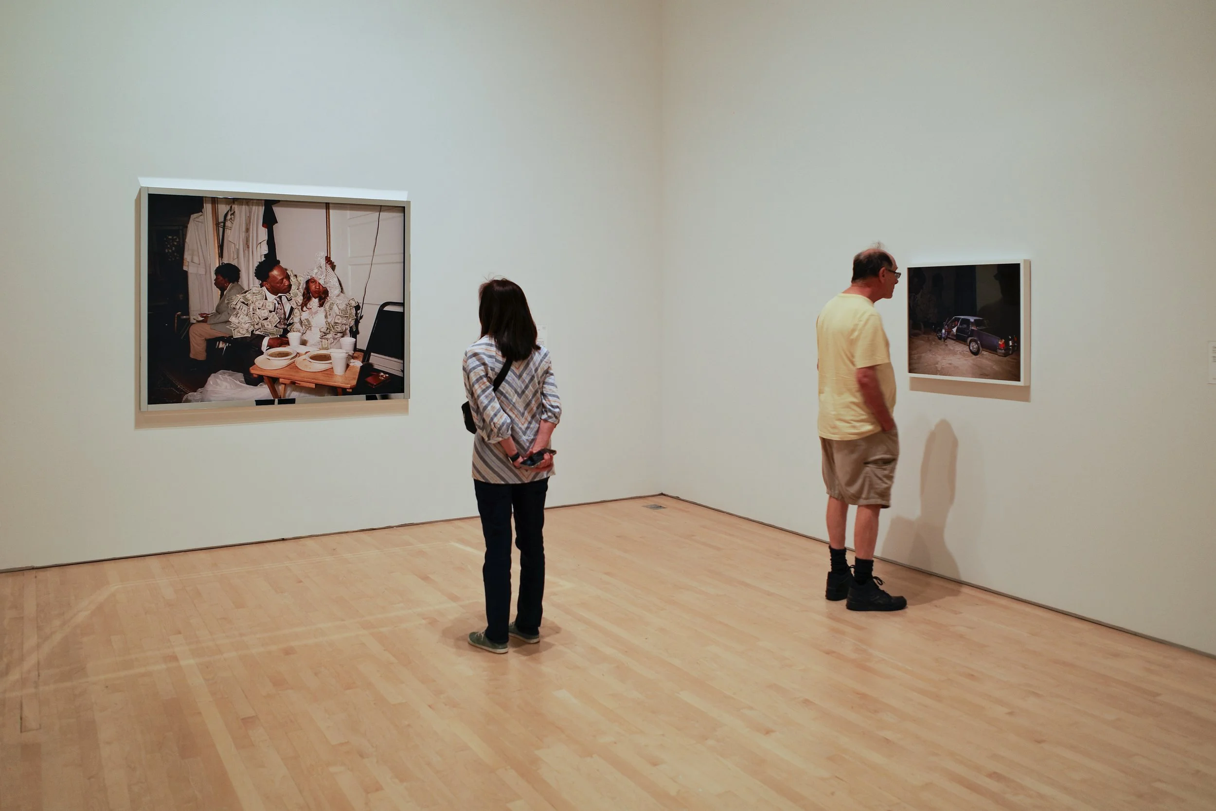People viewing photographs in an art gallery with light-colored walls and wooden floor.
