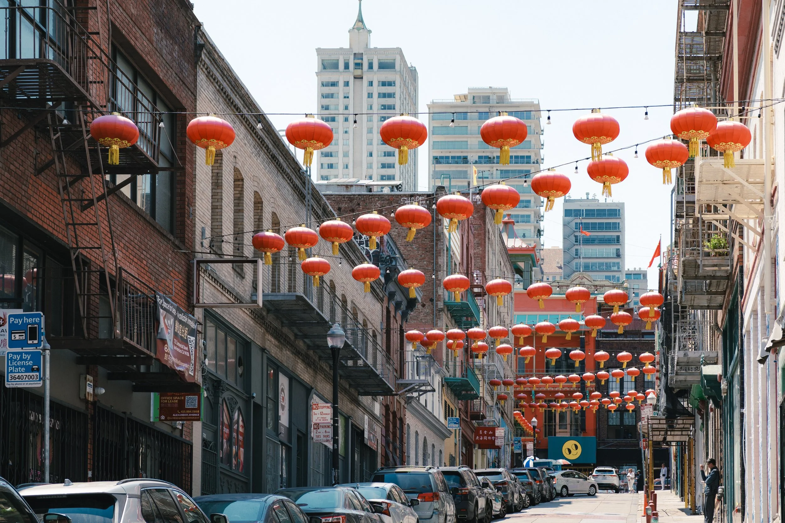City street decorated with numerous red Chinese lanterns hanging overhead between buildings in an urban area.