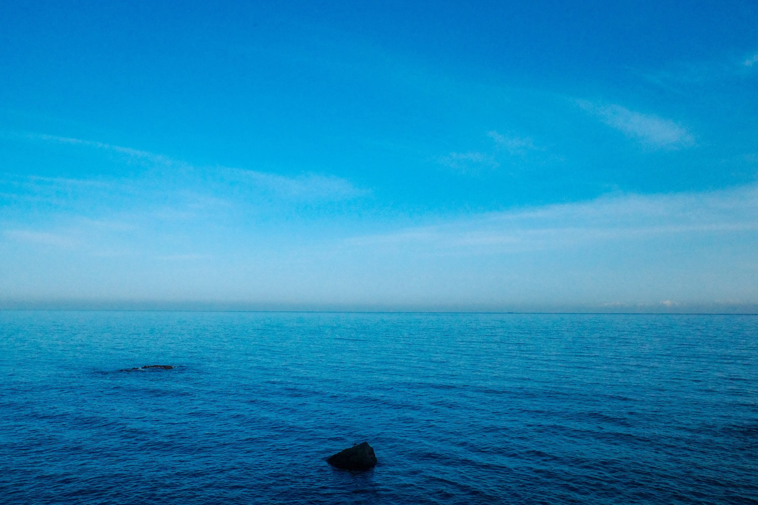 Calm ocean waters with a clear blue sky and a few clouds in the distance.