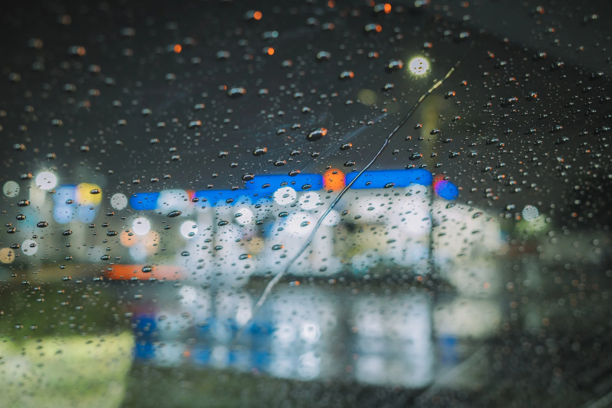 Rain drops on a car window at night with colorful blurry city lights in the background.