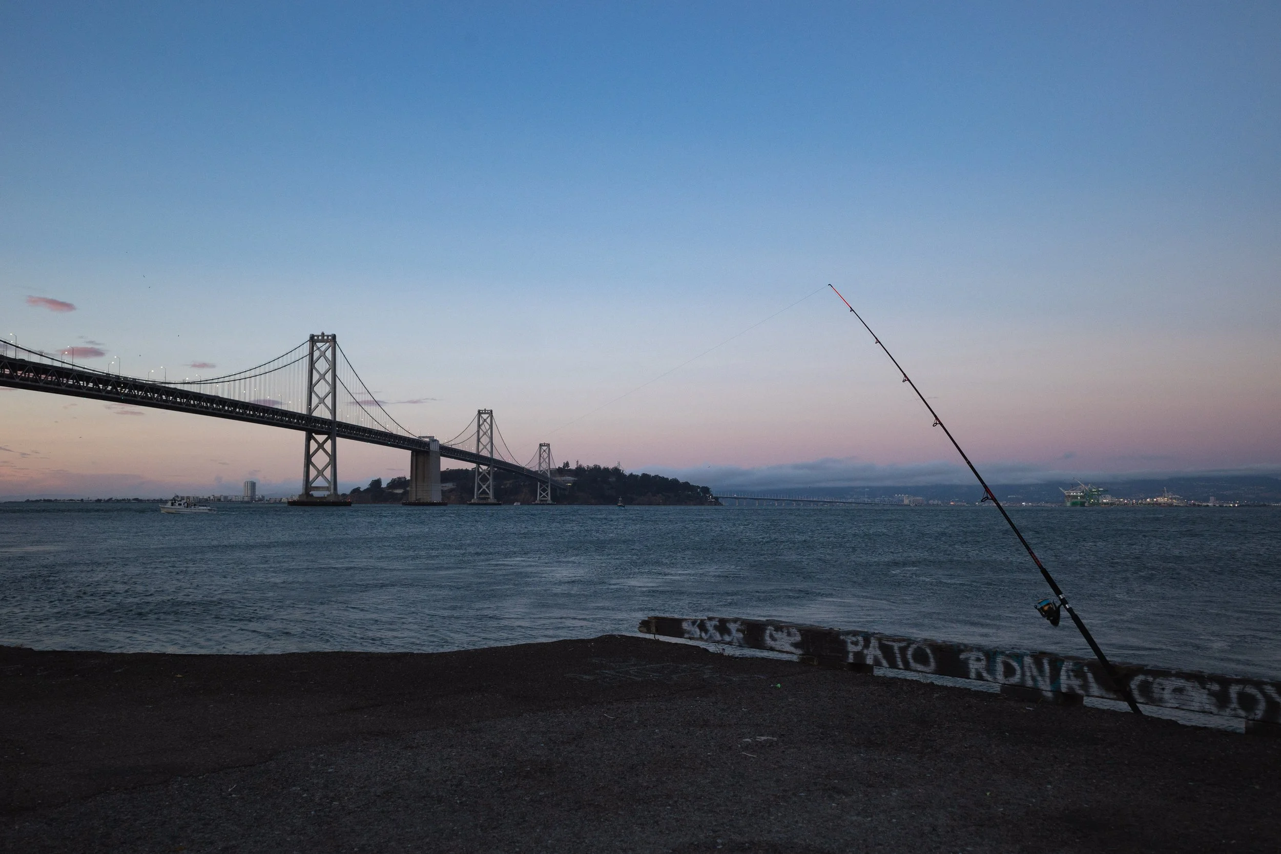 A bridge over water with a fishing rod in the foreground during sunset or dawn.