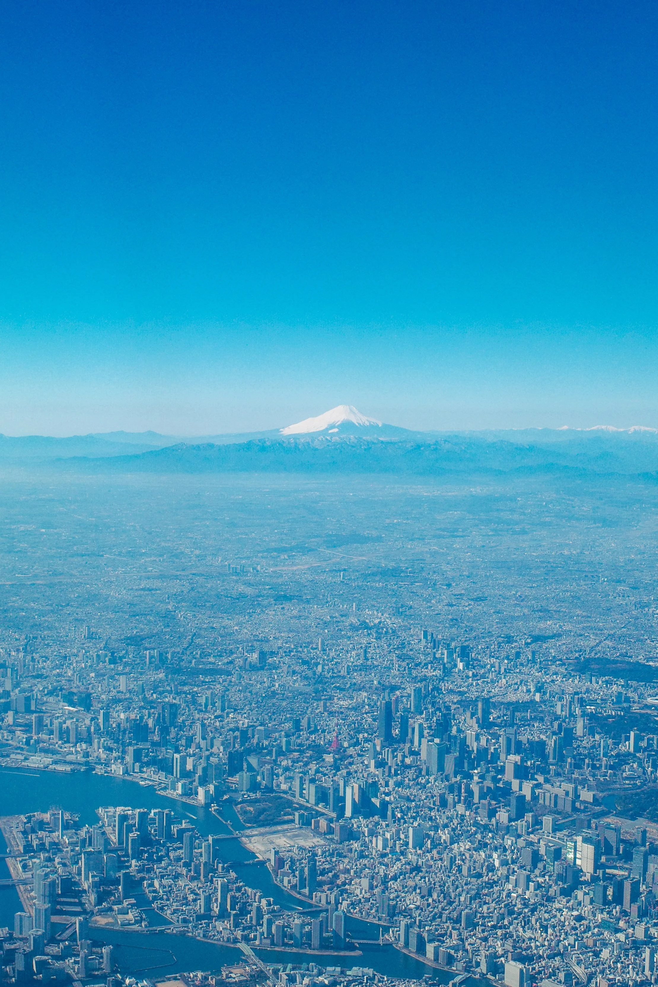 Aerial view of a city with a snow-capped mountain in the background under a clear blue sky.