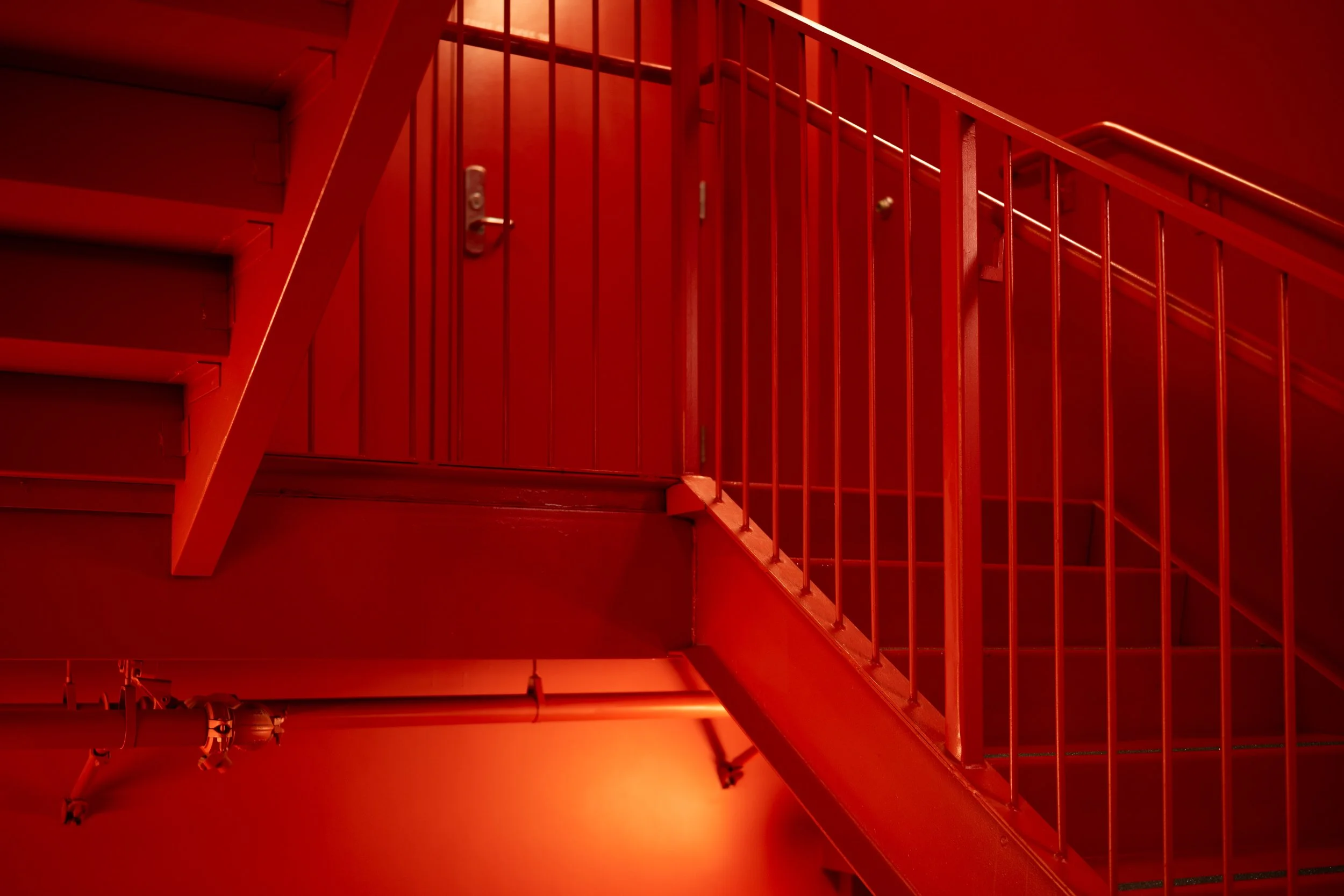 A red-painted staircase with a metal handrail and support beams, viewed from below, in a modern building.