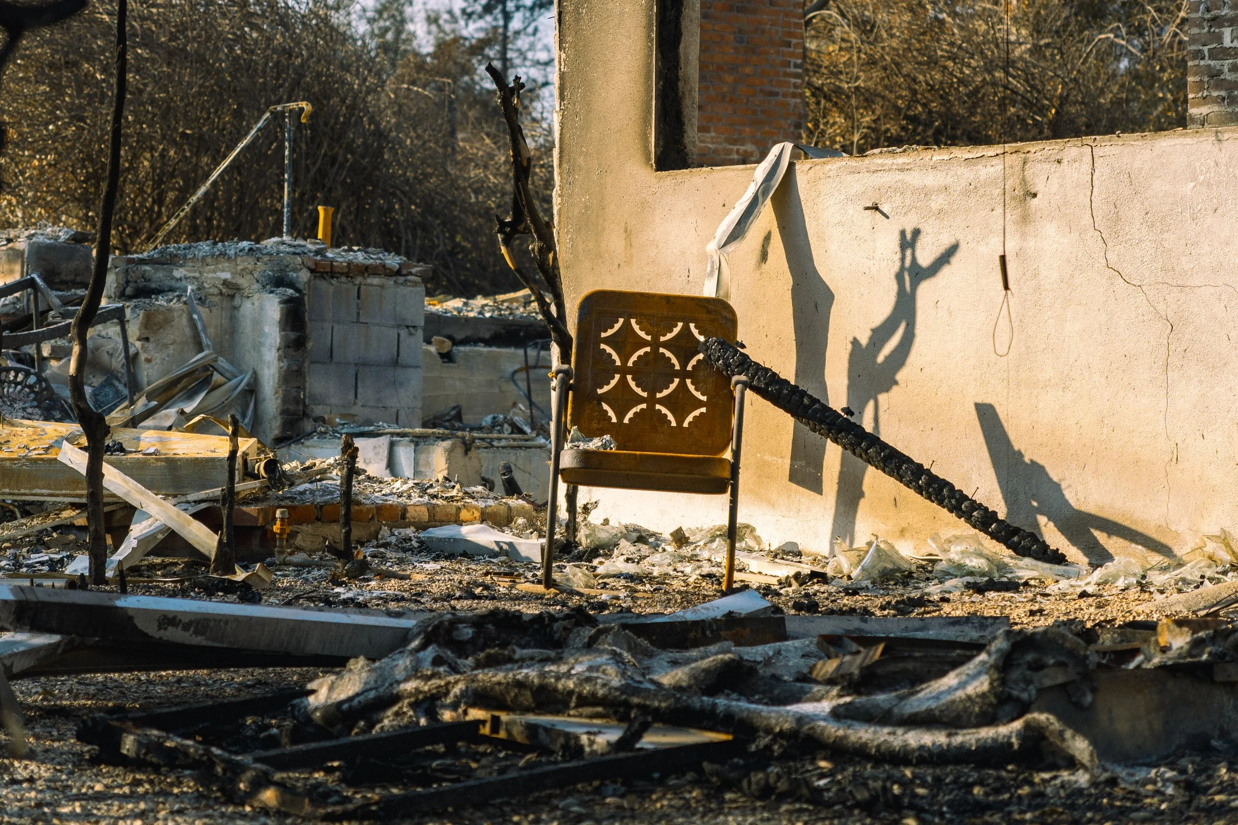 Scene of burnt remains with charred debris, a broken chair, and a damaged wall, indicating recent fire damage.