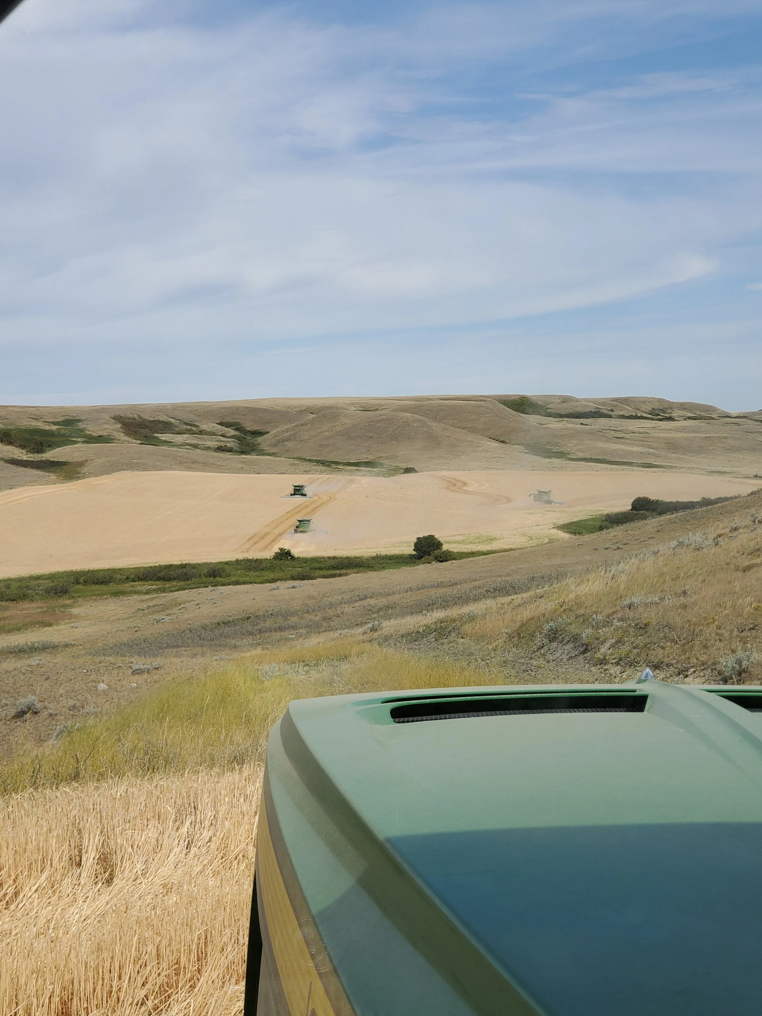 Looking out from a vehicle at a landscape of rolling hills, fields, and a partly cloudy sky.