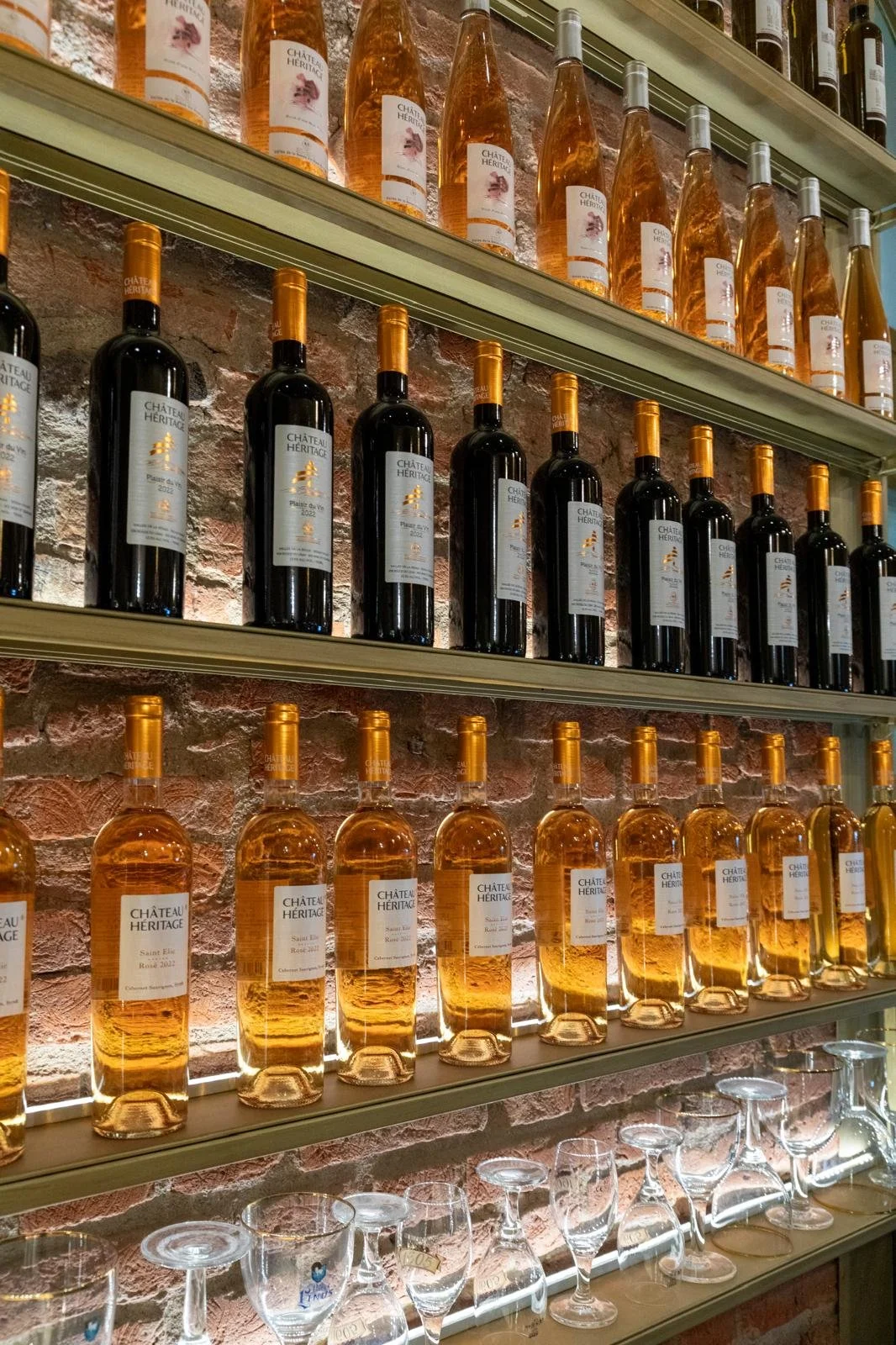 Scaffali con bottiglie di vino rosso e rosé, con bicchieri da vino sottostanti, in una enoteca o ristorante.