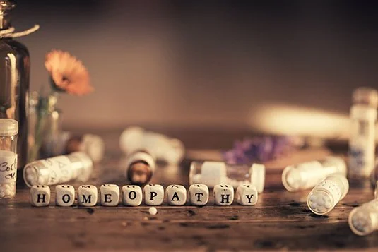 Homeopathy capsules and bottles with flowers on a wooden surface.