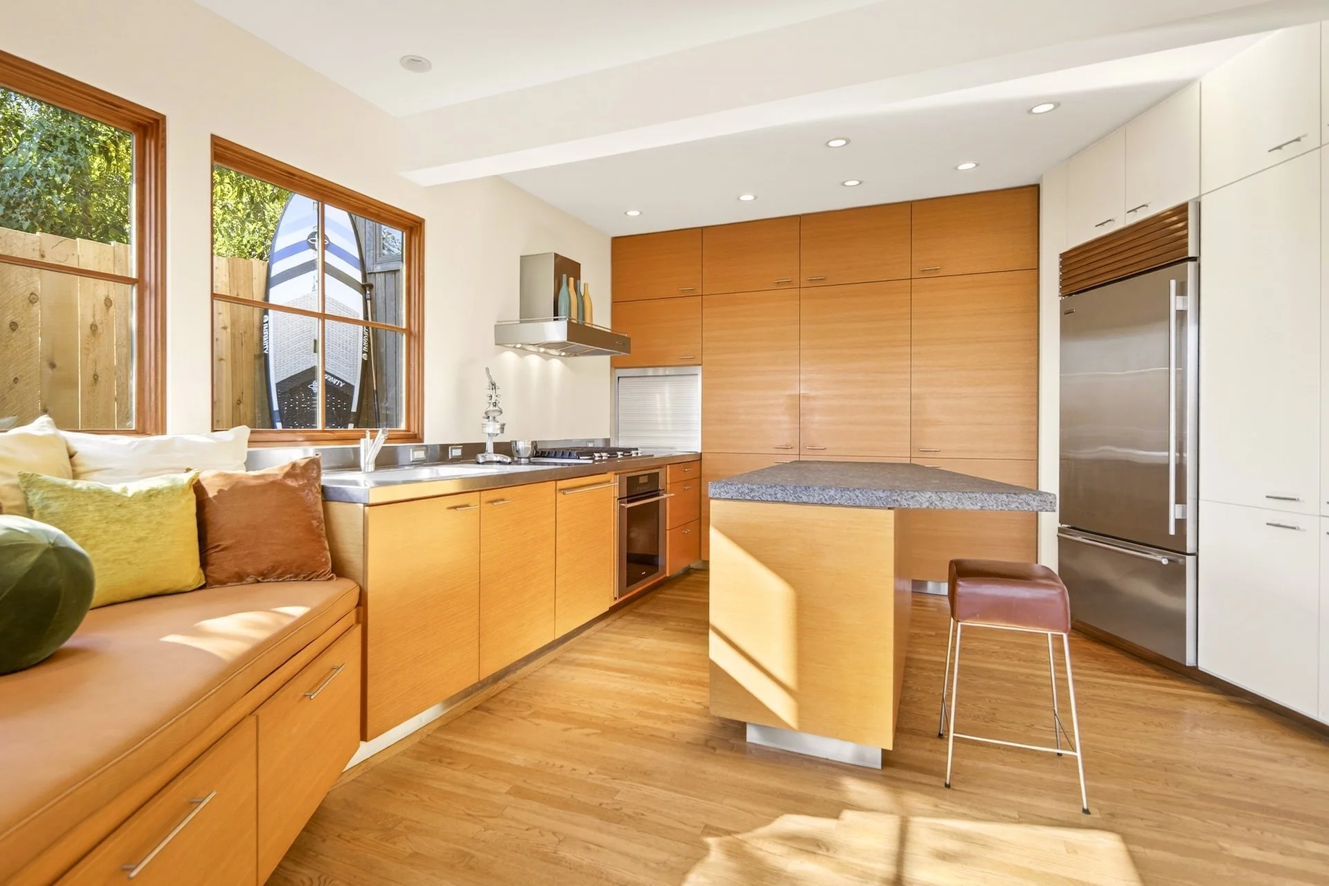 Modern kitchen with wooden cabinets, stainless steel appliances, granite counter island, large windows, and hardwood floors.